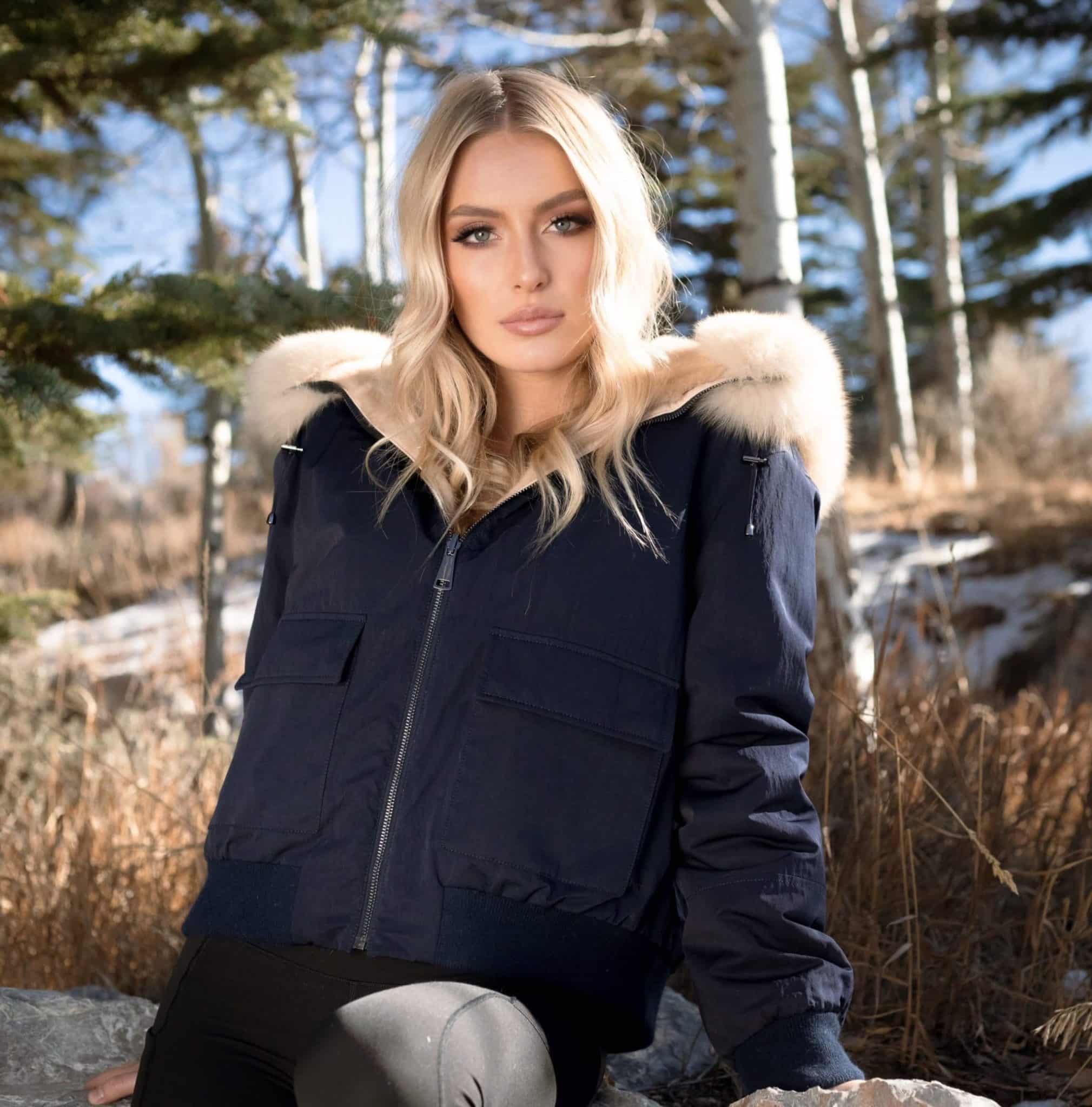 Frontal view of a woman in a fur coat with the rainwear side out sitting in a field.