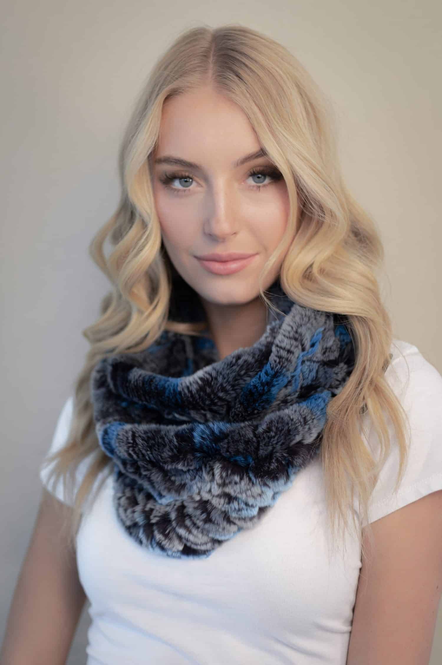 Frontal view of a woman in a blue chinchilla rex fur infinity scarf standing in front of a grey background.