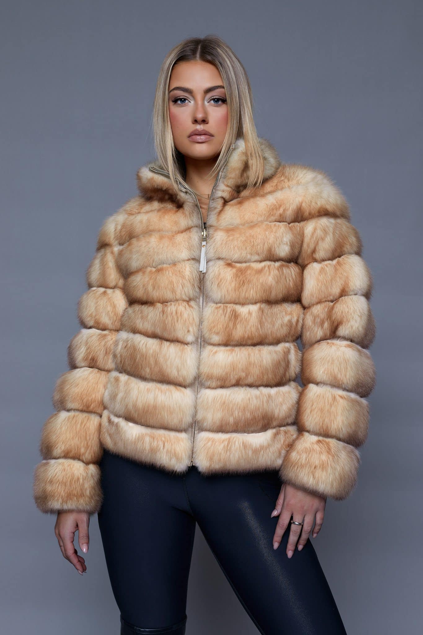 Frontal view of a woman in a fur coat standing in front of a grey background.