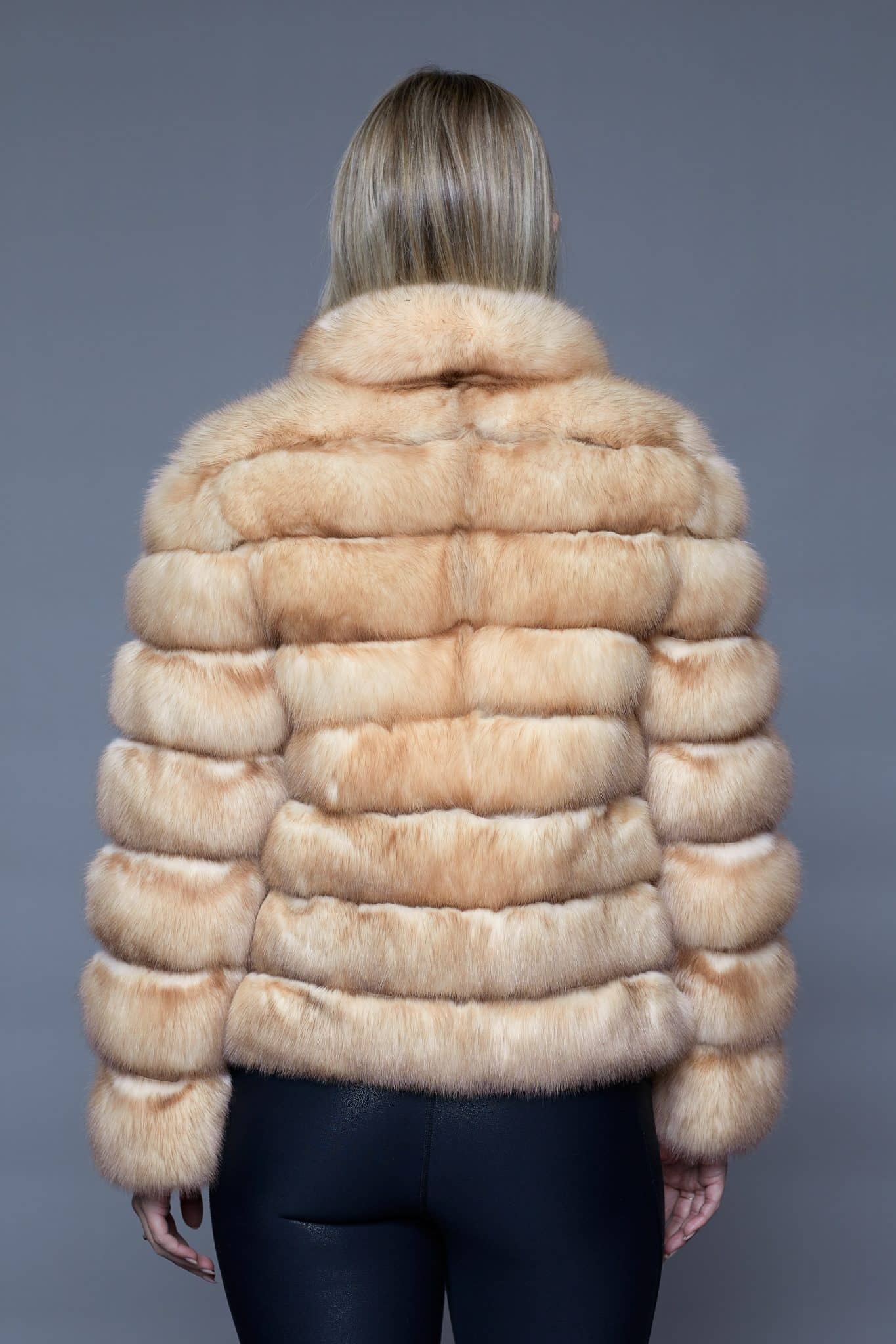 Rear view of a woman in a fur coat facing a grey background.