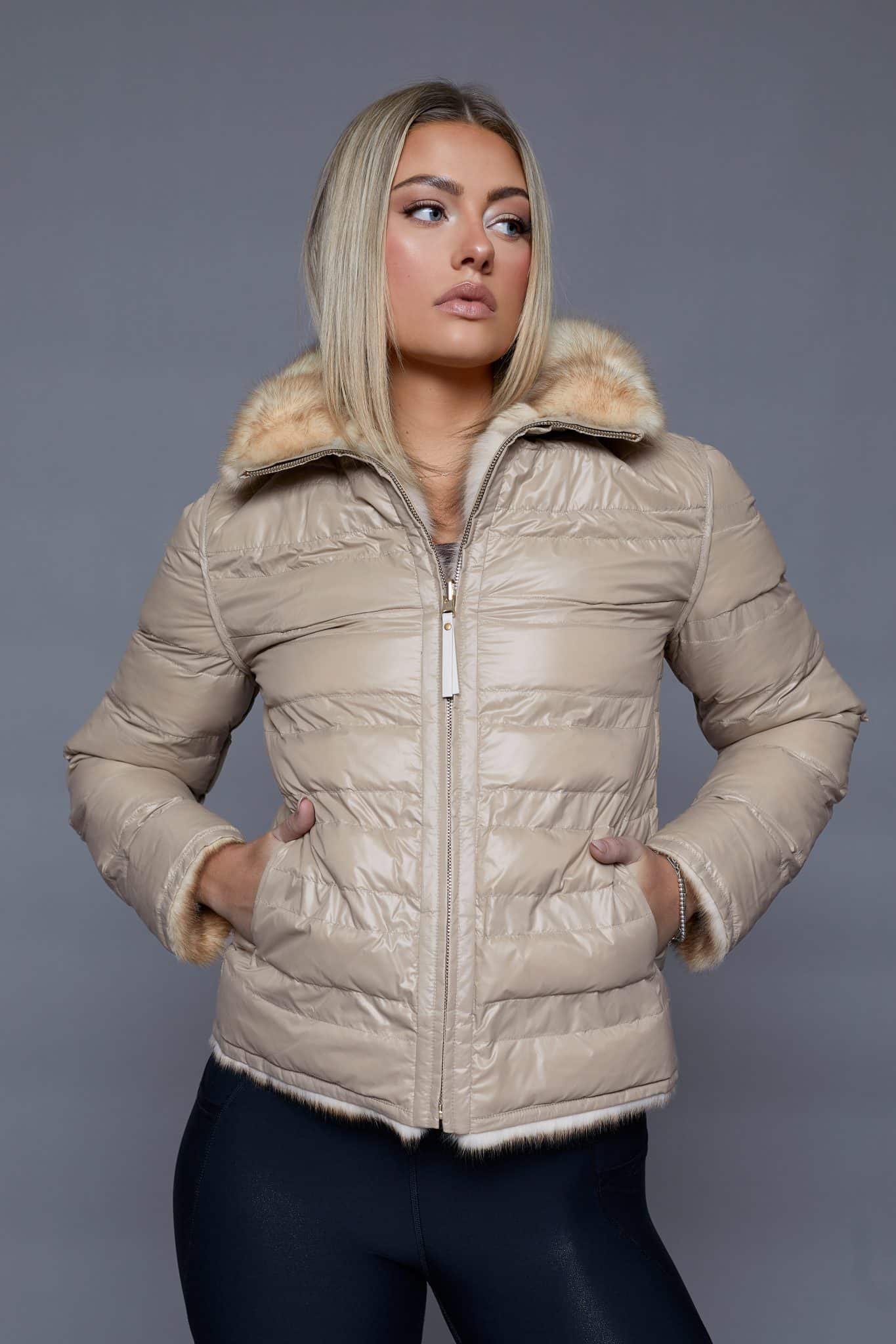 Frontal view of a woman in a reversible fur coat with the shell side out standing in front of a grey background.