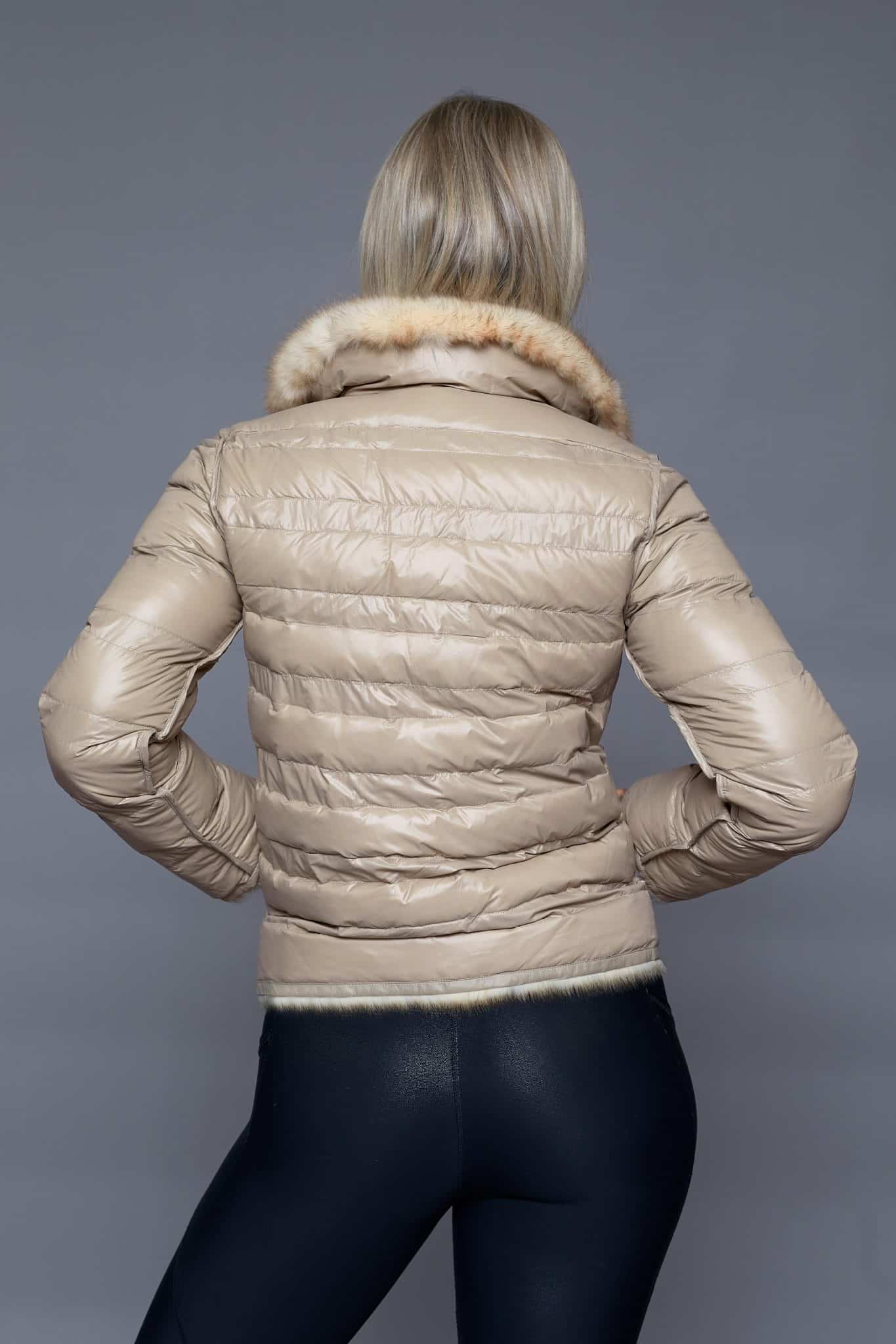 Rear view of a woman wearing a reversible fur coat with the shell side out facing a grey background.