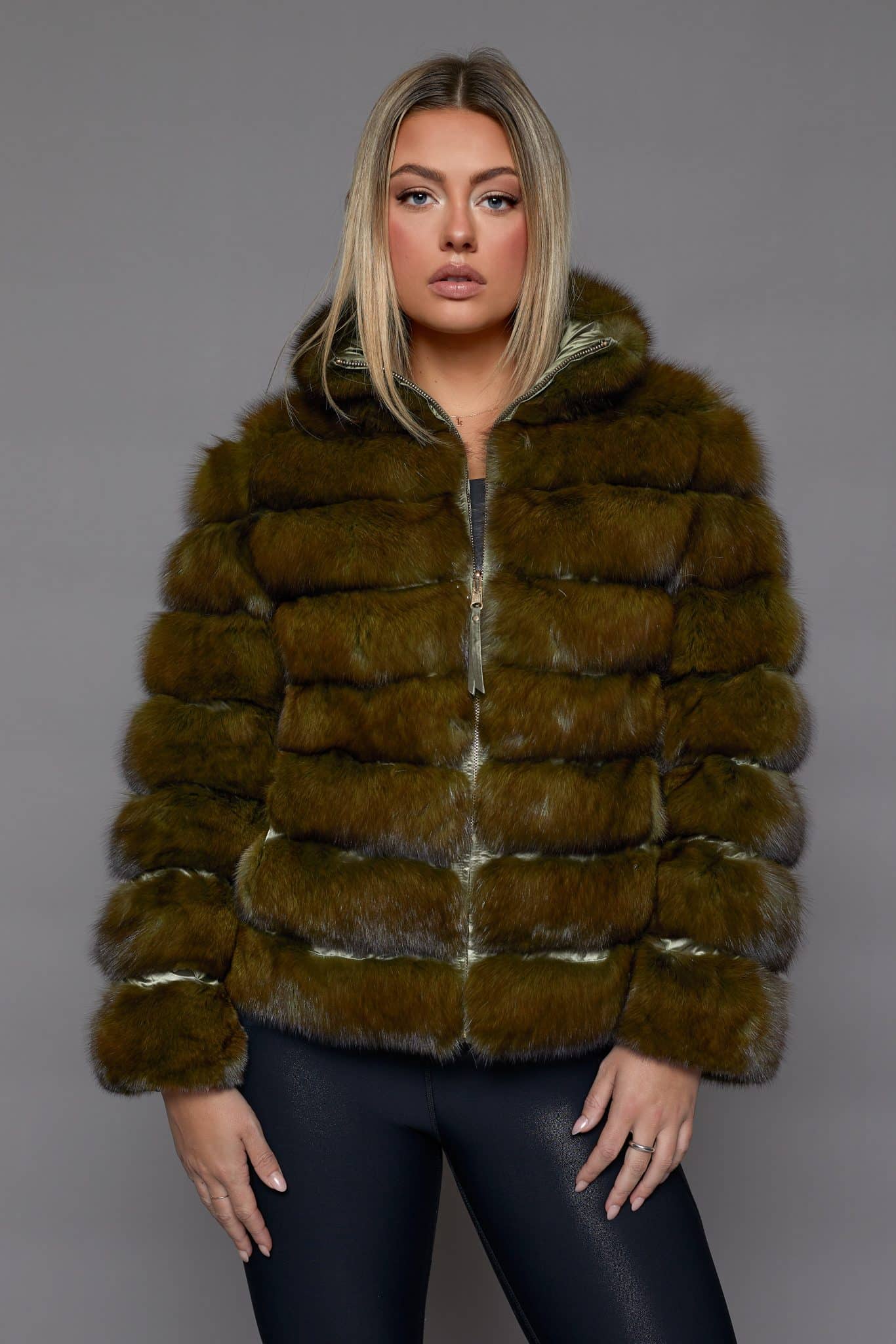 Frontal view of a woman wearing a fur coat standing in front of a grey background.