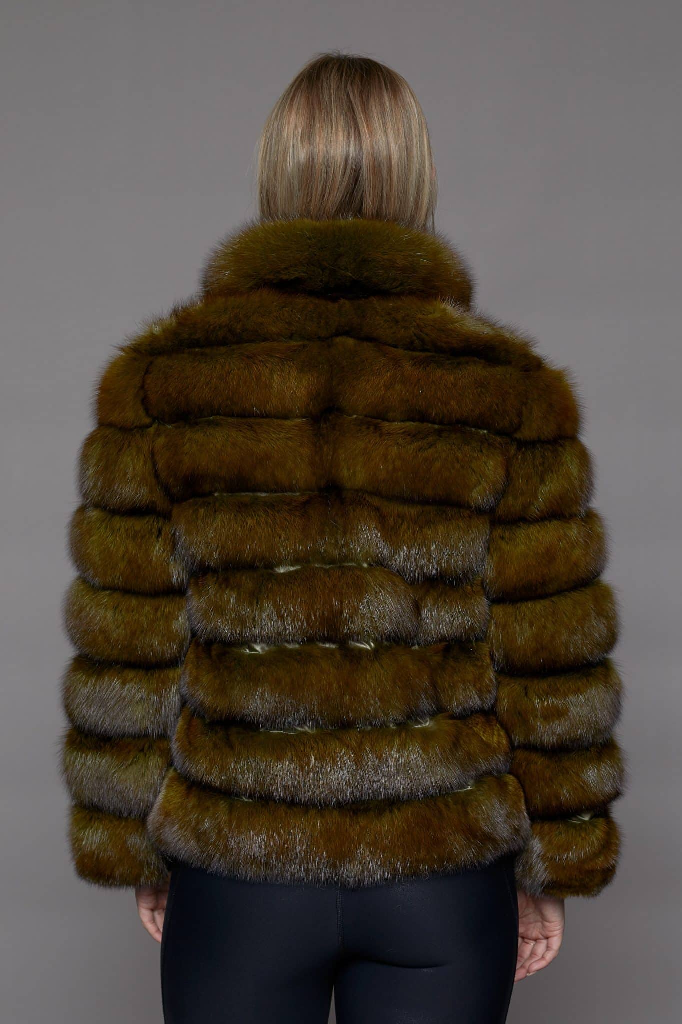 Rear view of a woman wearing a fur coat facing a grey background.