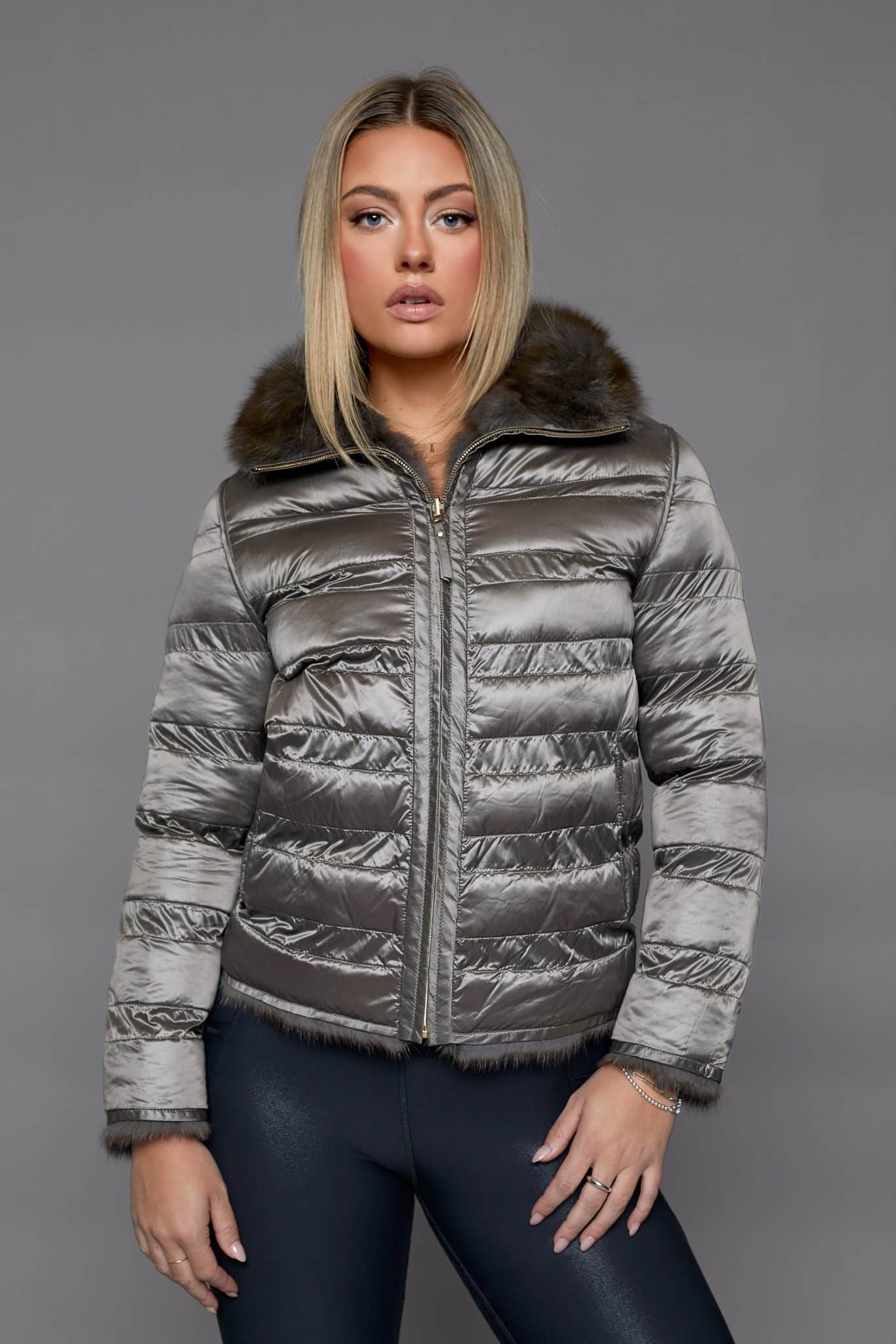 Frontal view of a woman wearing a reversible coat with the shell side out standing in front of a grey background.