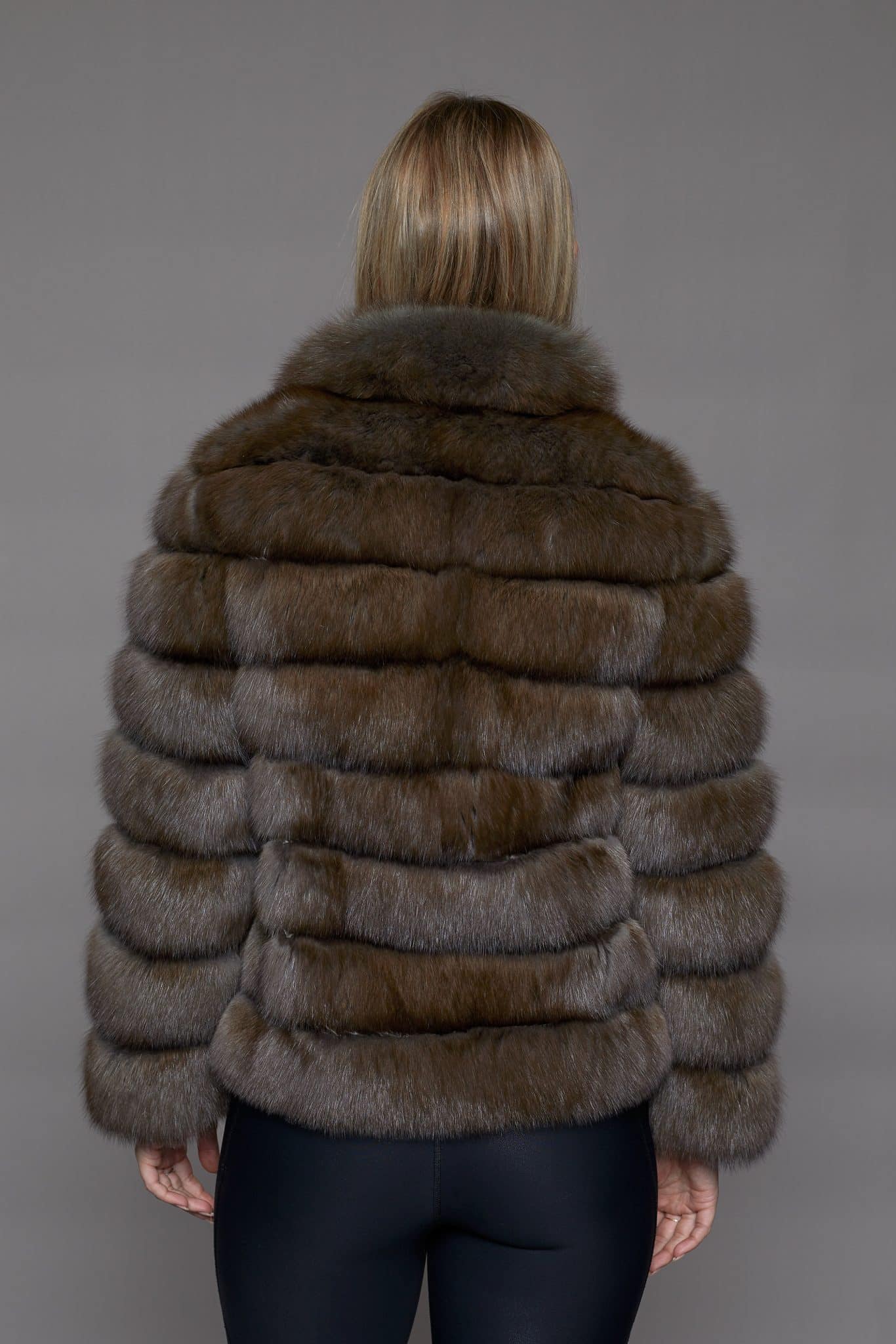 Rear view of a woman wearing a fur coat facing a grey background.