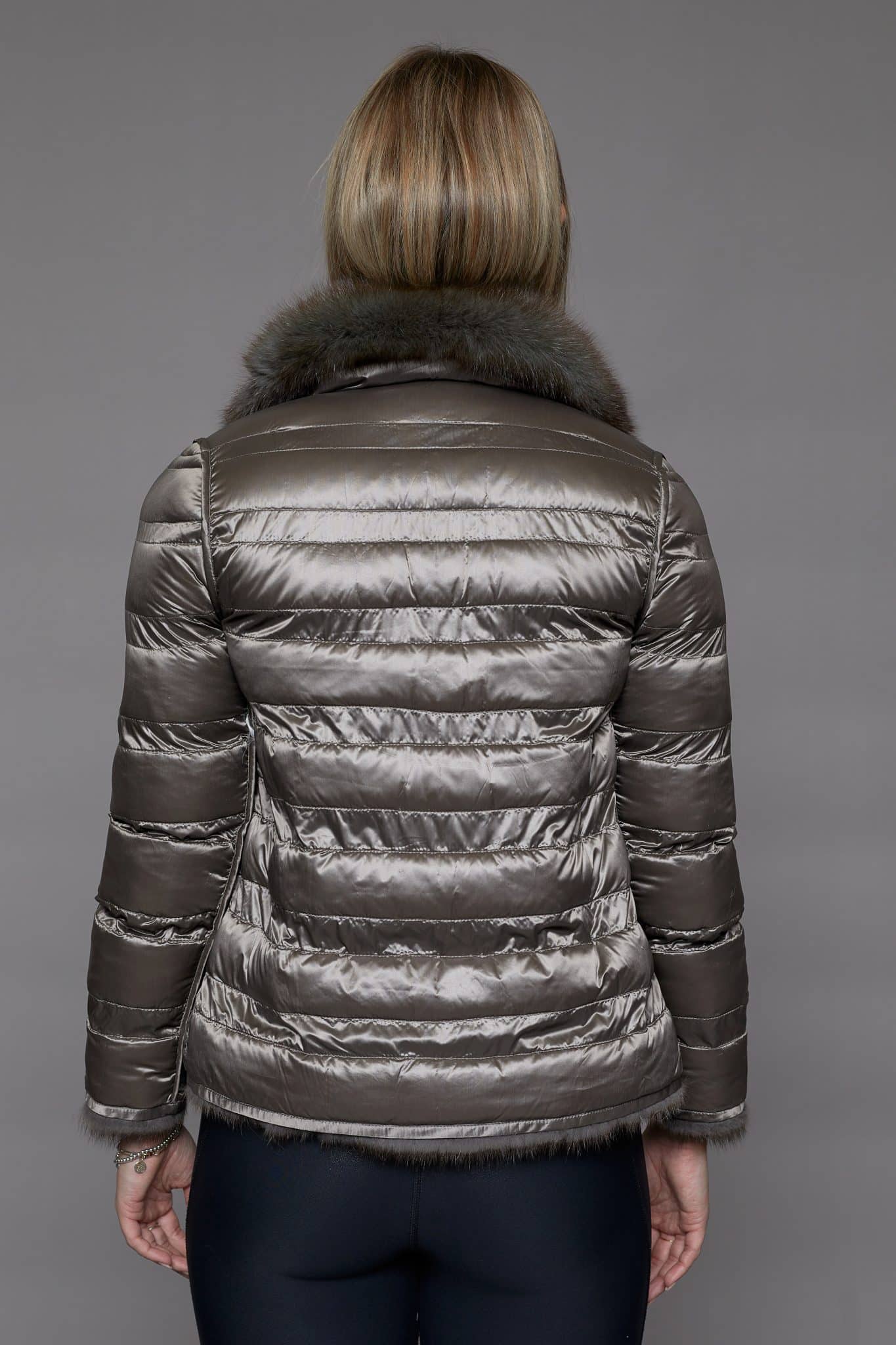 Rear view of a woman in a reversible coat with the shell side out facing a grey background.