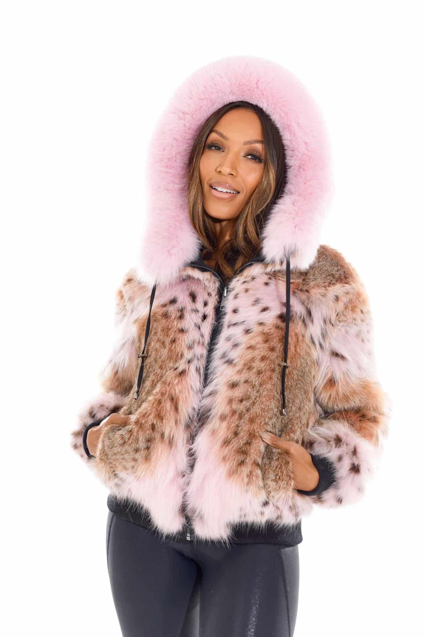 Frontal view of a woman wearing a fur coat with the hood up and her hands in the pockets standing in front of a white background.