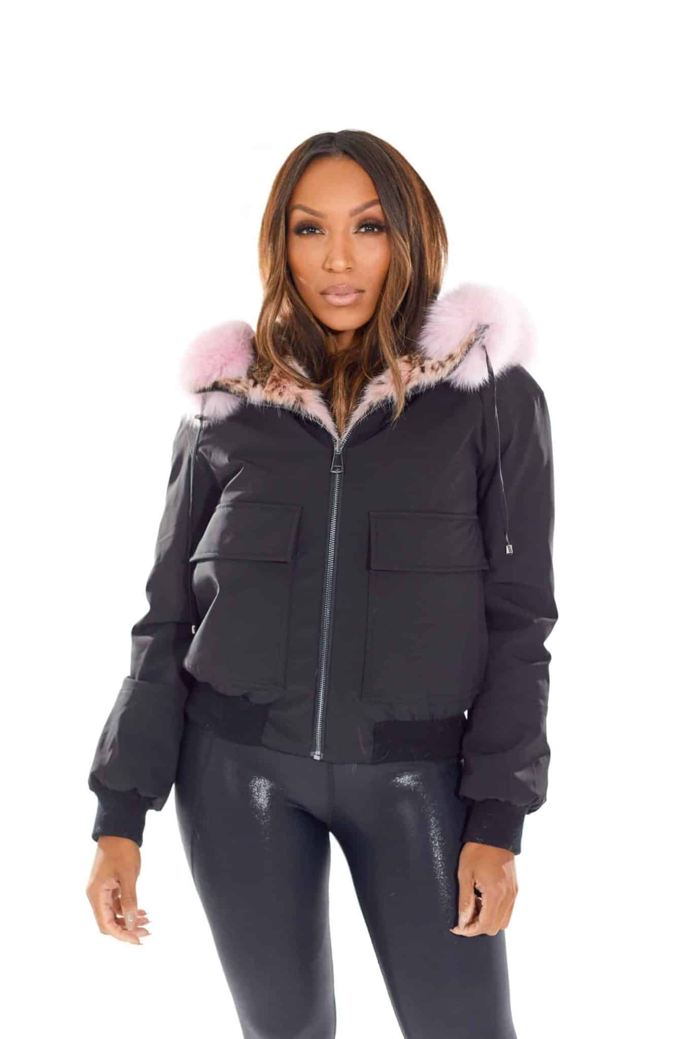 Frontal view of a woman wearing a reversible fur coat with the shell side out and hood down and coat zipped up standing in front of a white background.