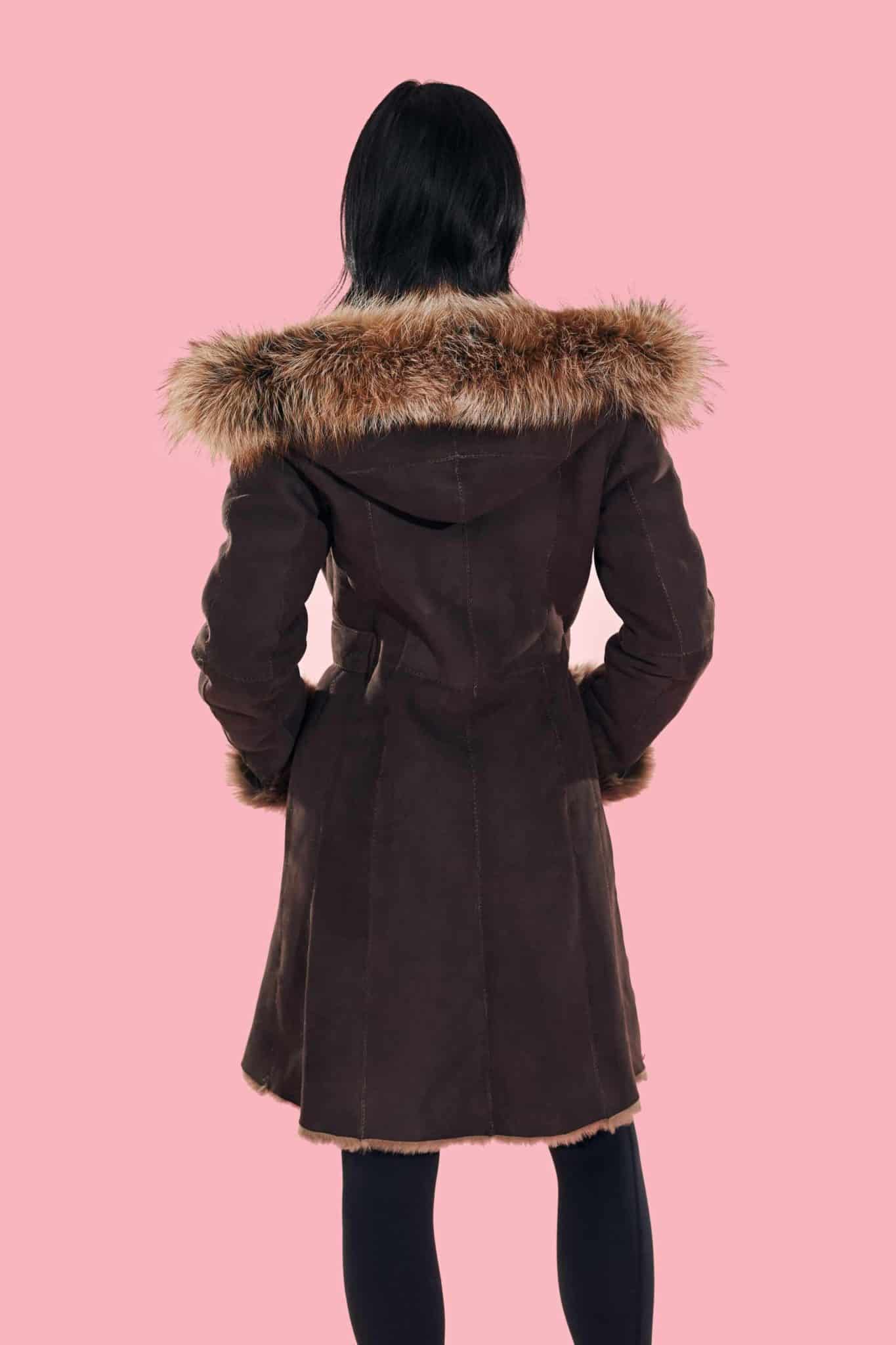 Rear view of a woman wearing a coat with the hood down facing a pink background.