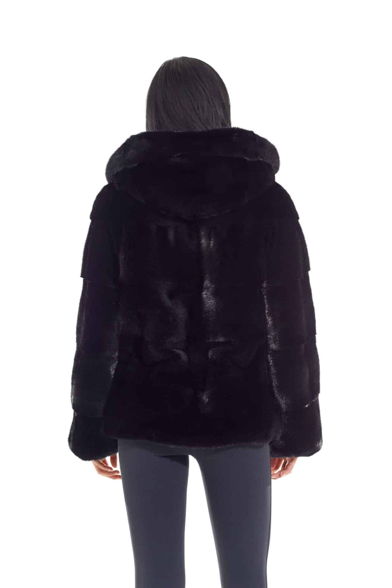 Rear view of a woman wearing a mink fur jacket with the fur side out facing a white background. The woman's hands are at her side.