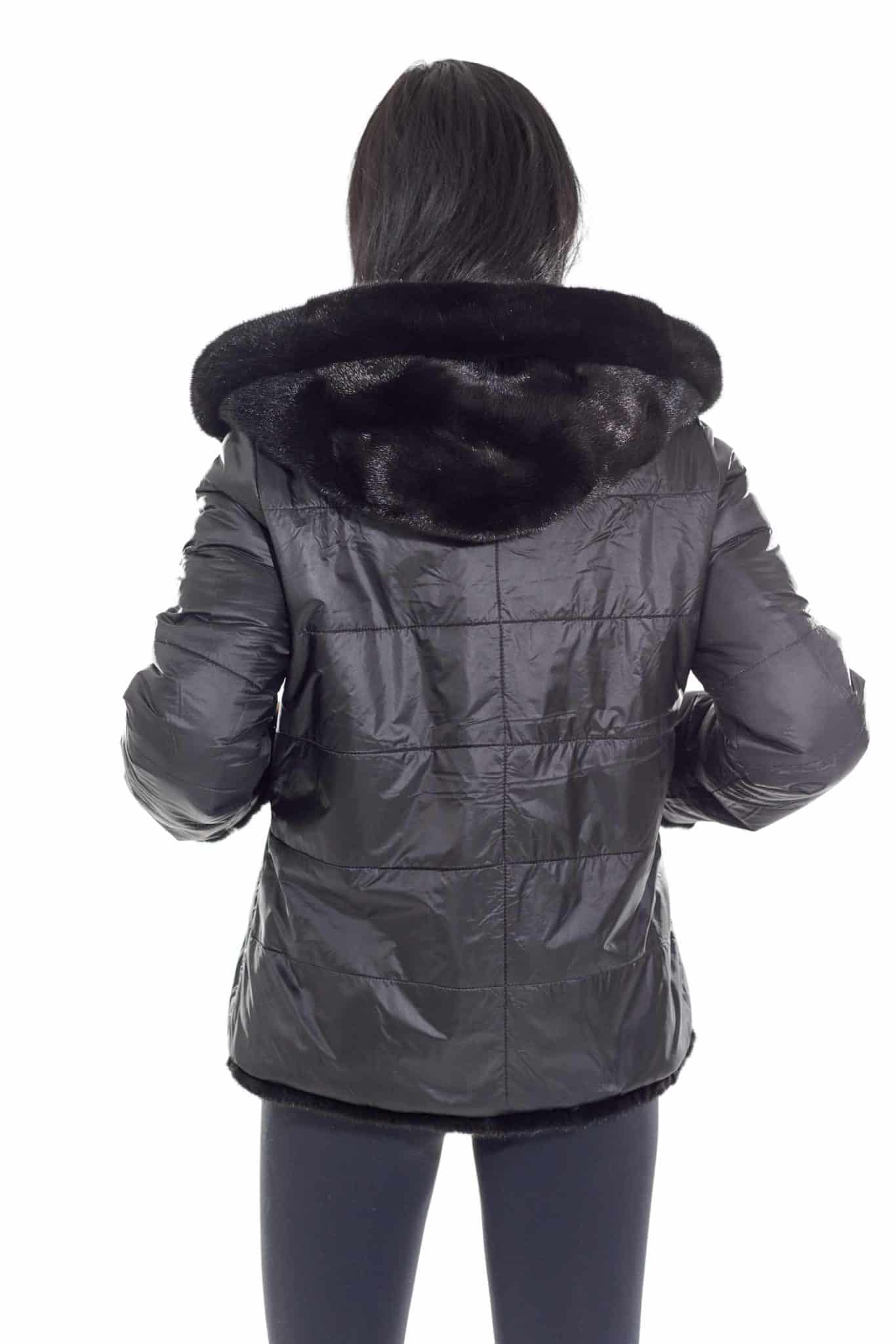 Rear shot of a woman wearing a mink fur jacket with the fur side out facing a white background.