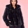 Frontal view of a woman wearing a fur coat with the hood down standing in front of a pink background.