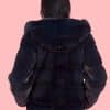 Rear view of a woman wearing a fur coat with the hood down facing a pink background.