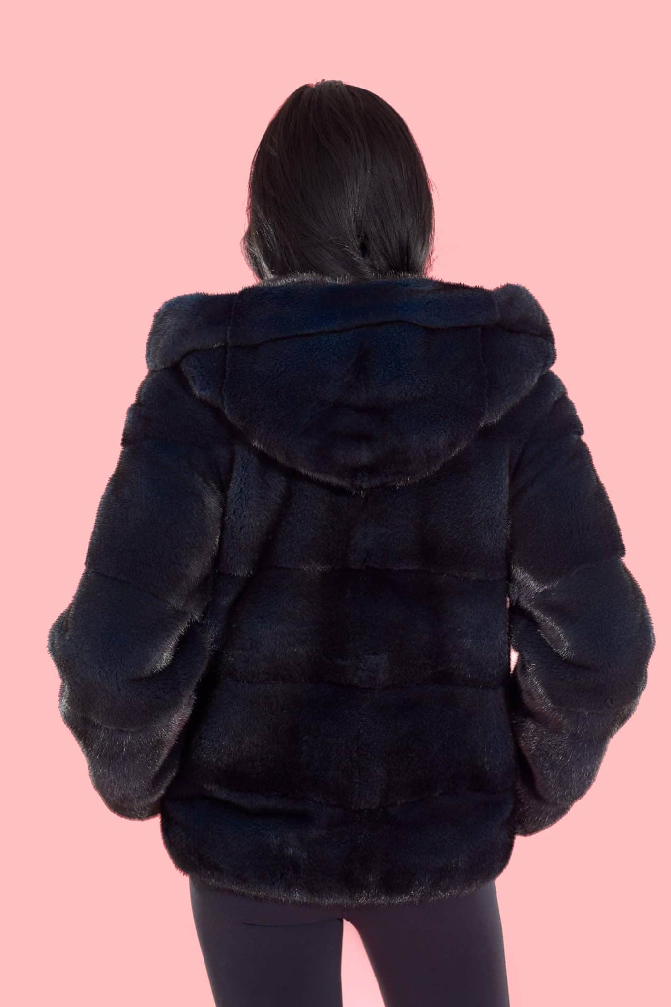 Rear view of a woman wearing a fur coat with the hood down facing a pink background.
