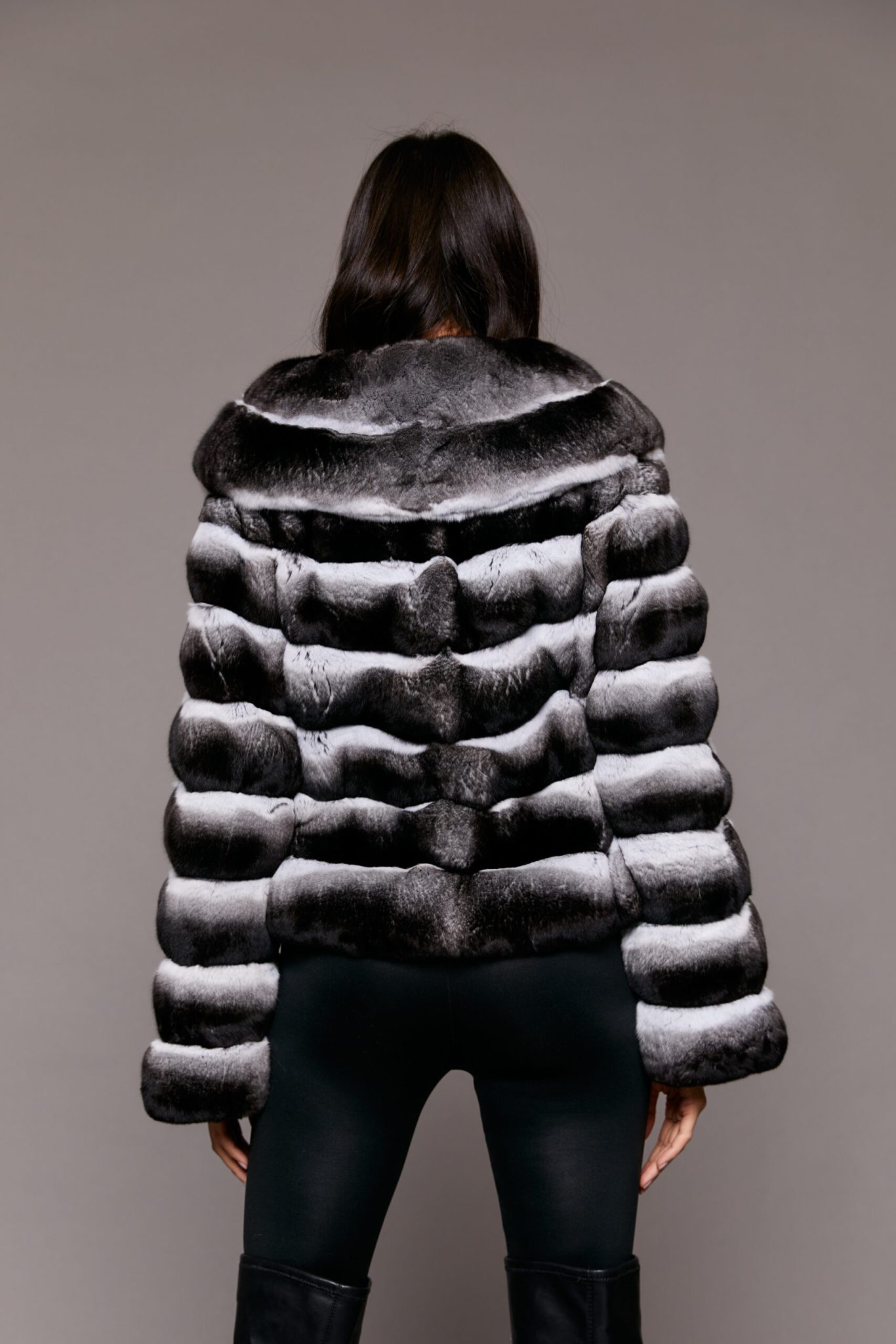 Rear view of a woman wearing a fur coat facing a grey background.