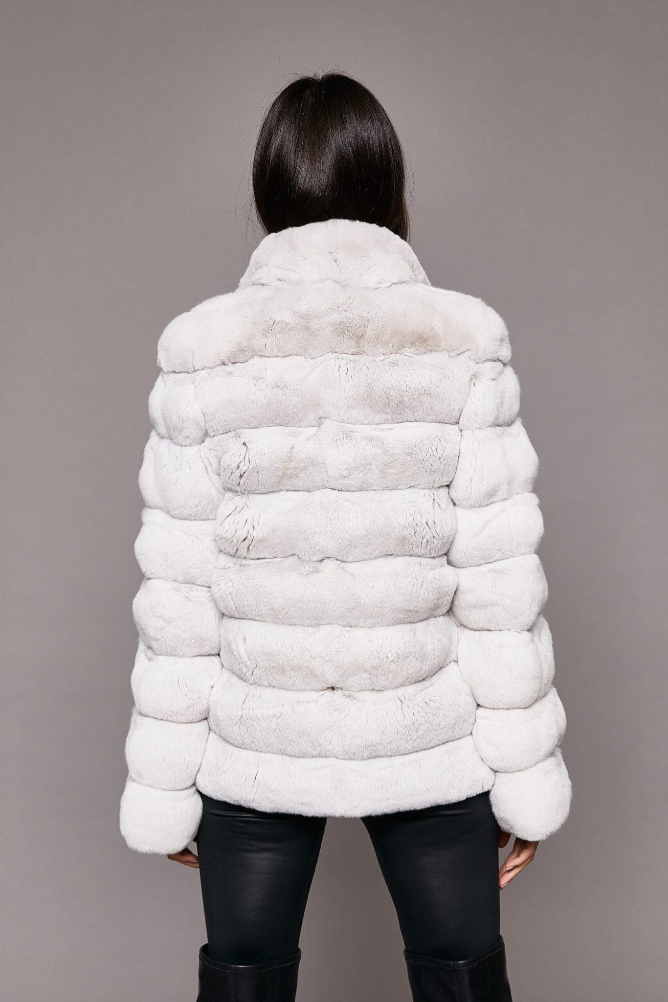 Rear view of a woman wearing a white genuine chinchilla coat standing in front of a seamless backdrop