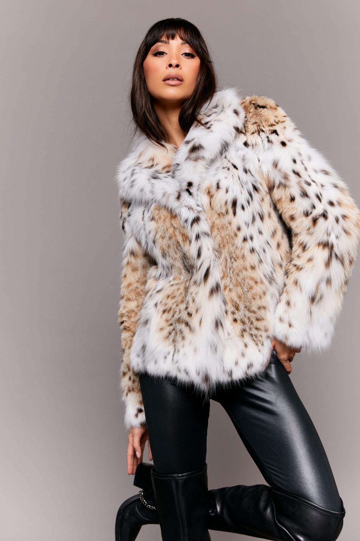 Frontal view of a woman wearing a lynx fur jacket posed in front of a grey background.