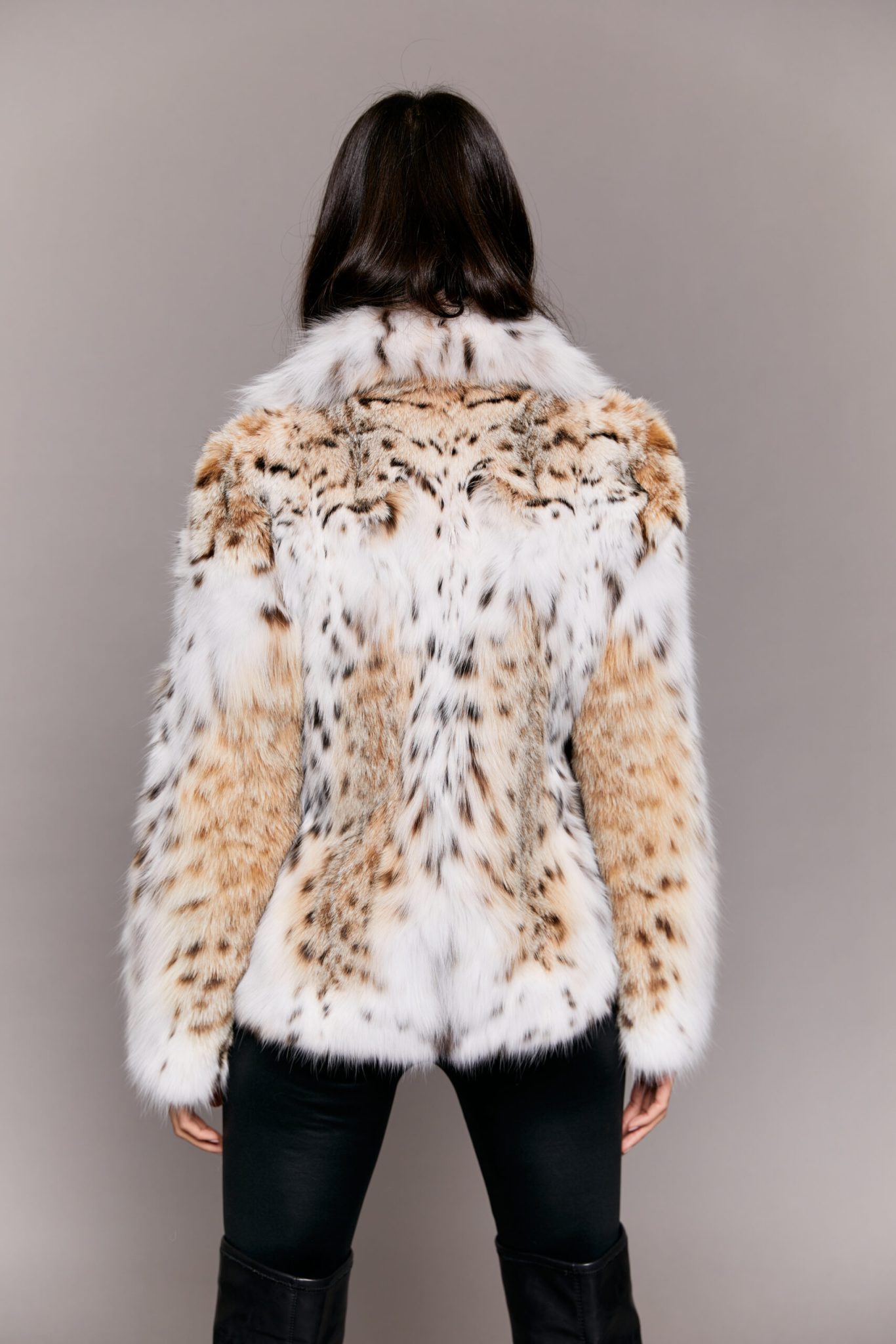Rear view of a woman wearing a lynx fur jacket facing a grey background.