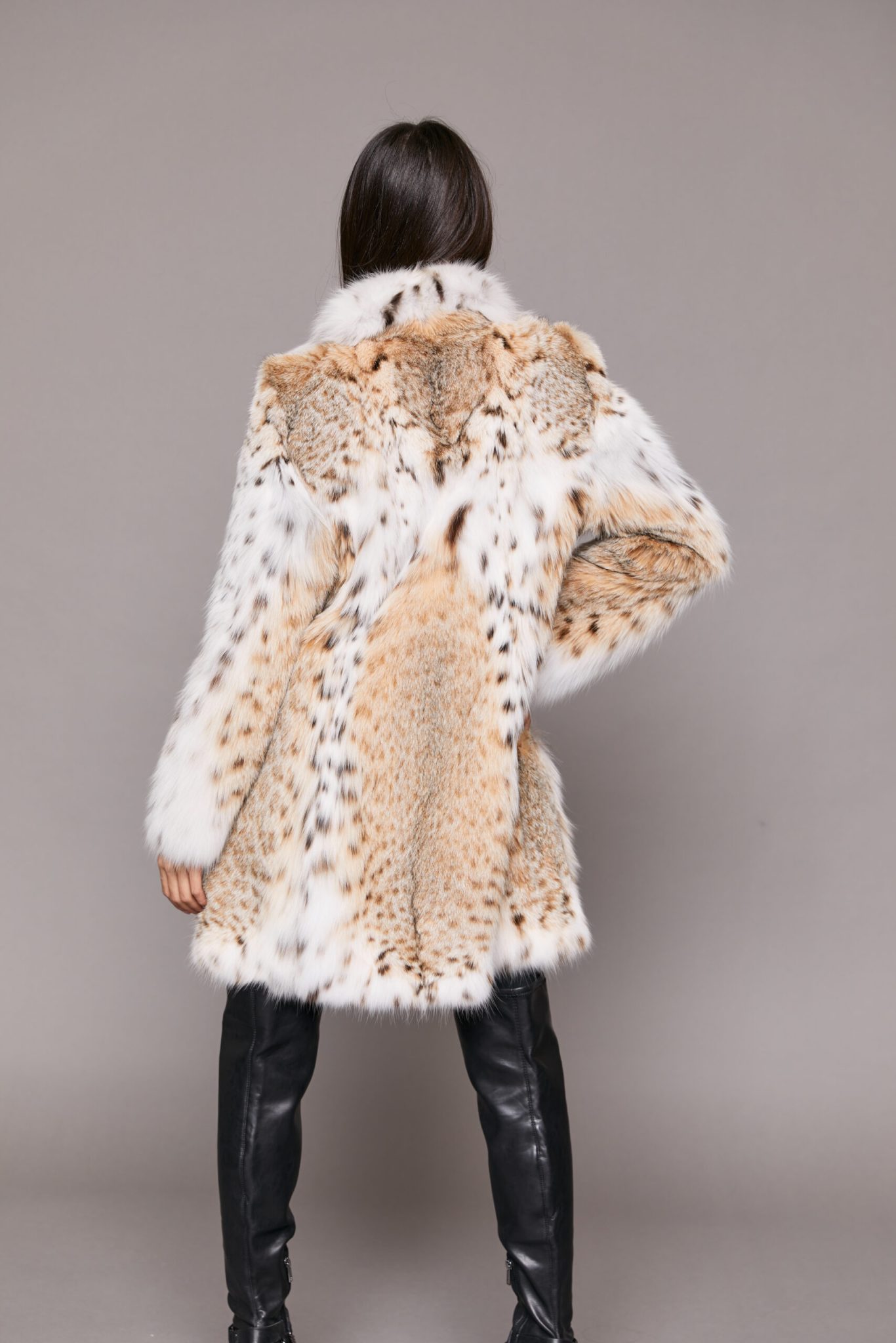 Rear view of a woman wearing a long fur coat facing a grey background.