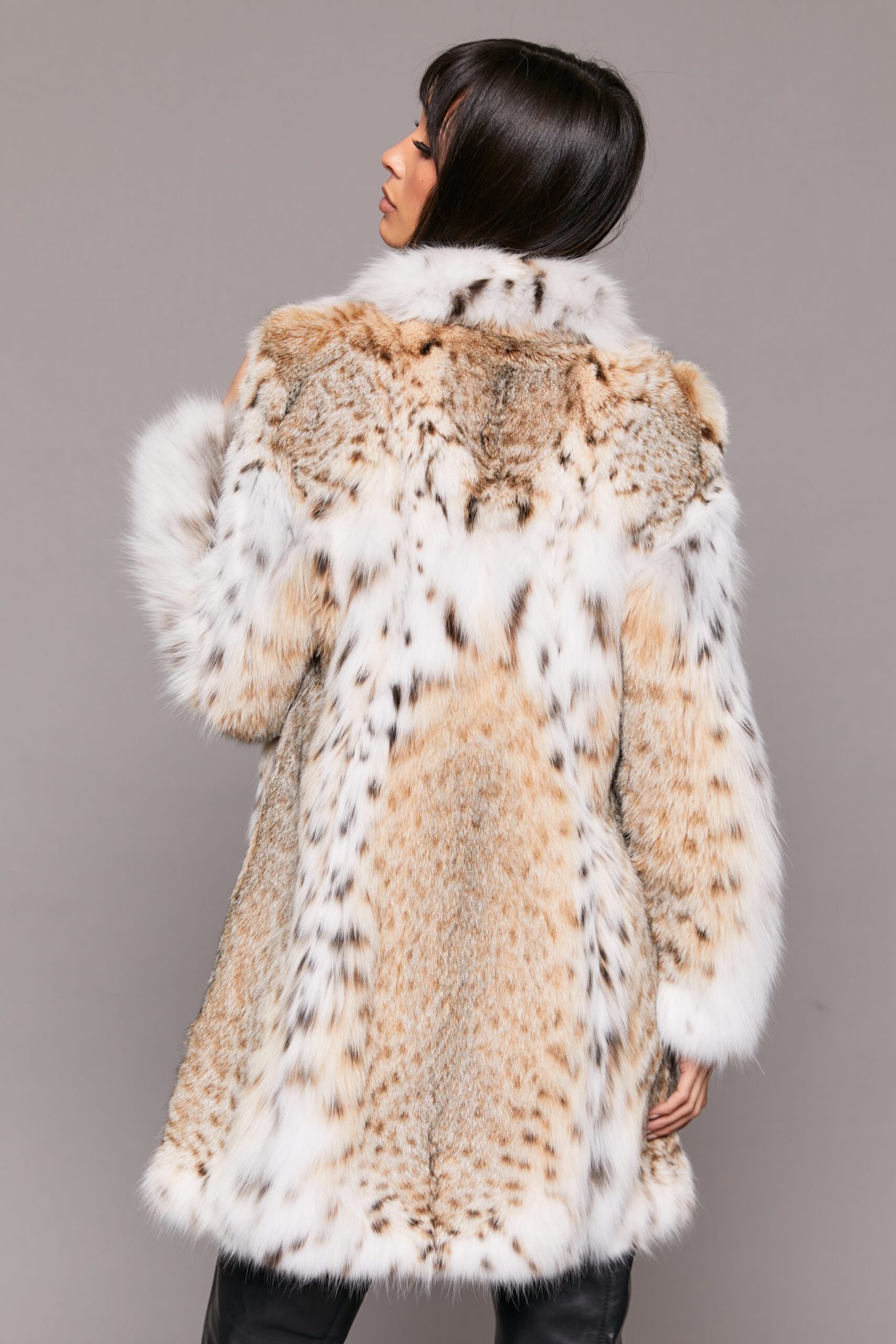 Rear view of a woman wearing a fur coat facing a grey background.