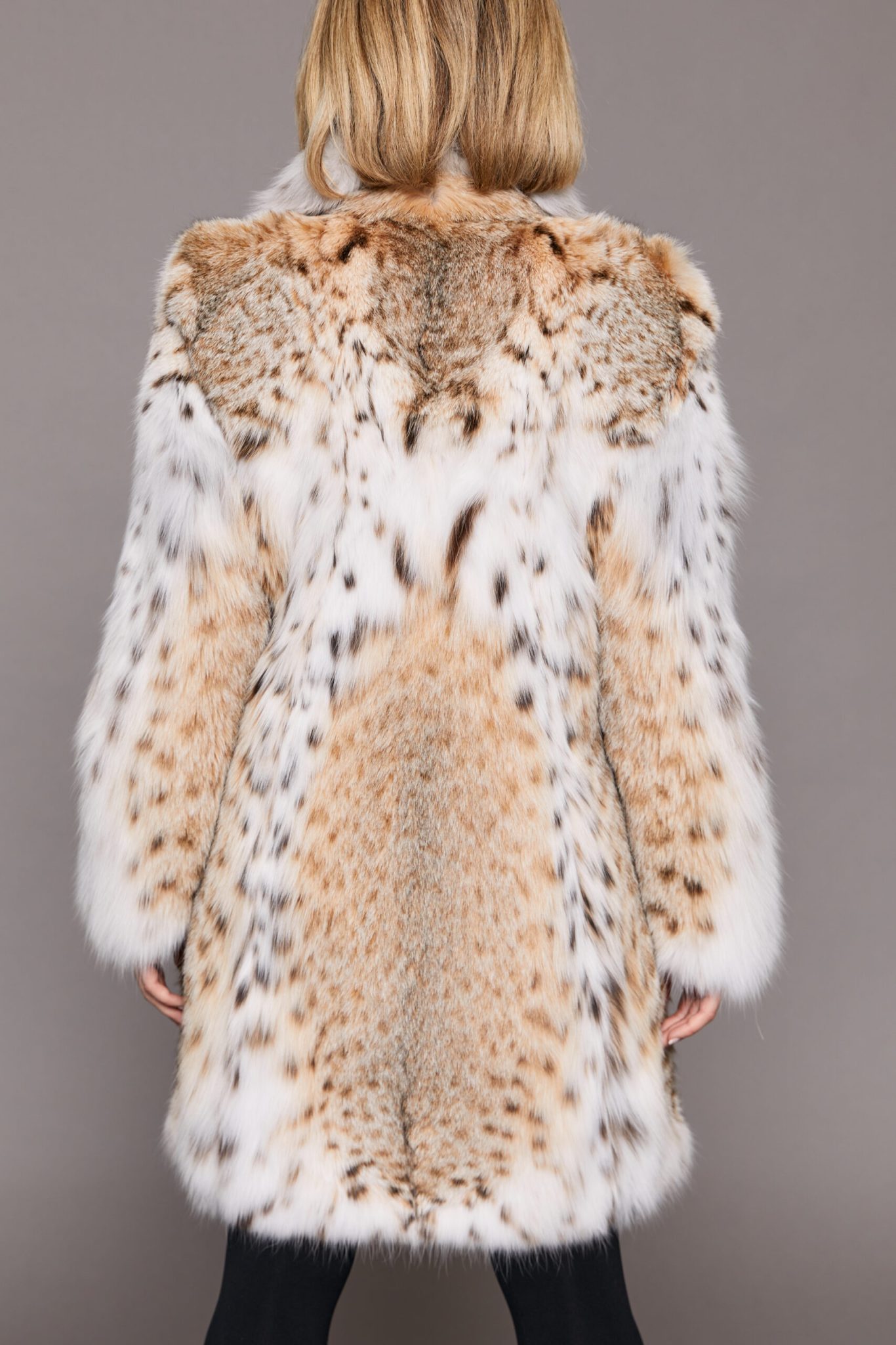 Rear view of a woman wearing a lynx fur jacket facing a grey background with her arms at her sides