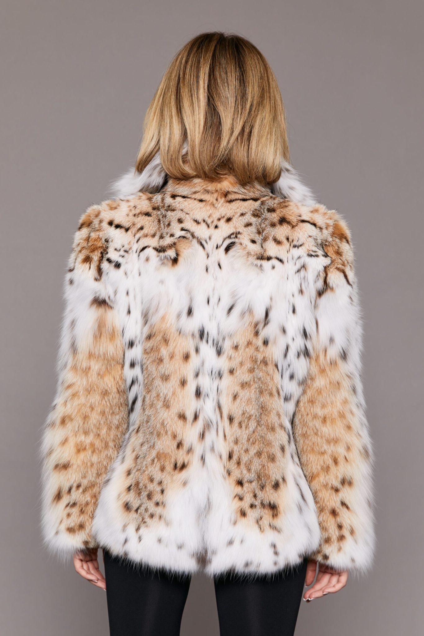 Rear view of a woman wearing a lynx fur jacket facing a grey background.