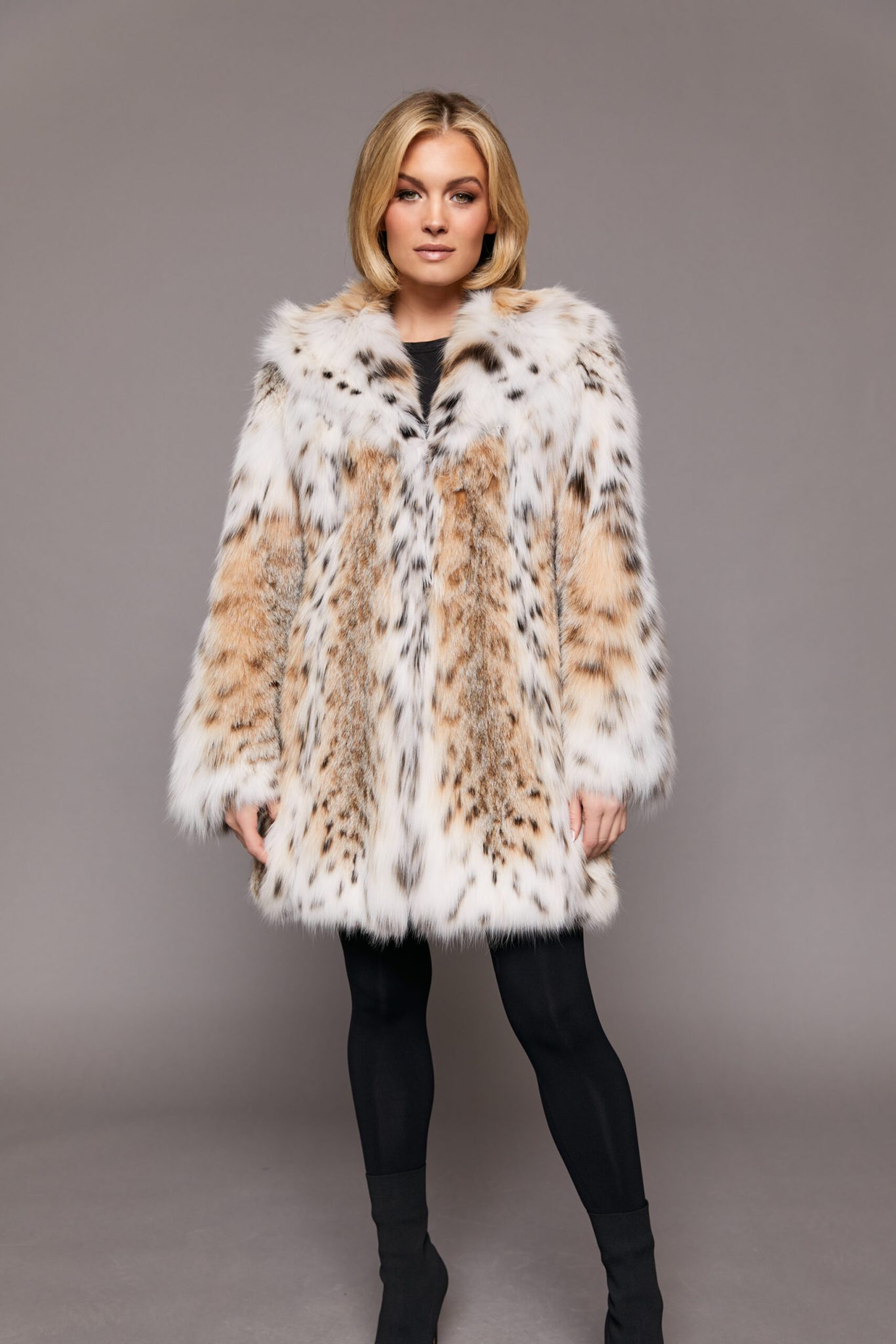 Frontal view of a woman wearing a fur coat standing in front of a grey background. The woman's arms are at her side.