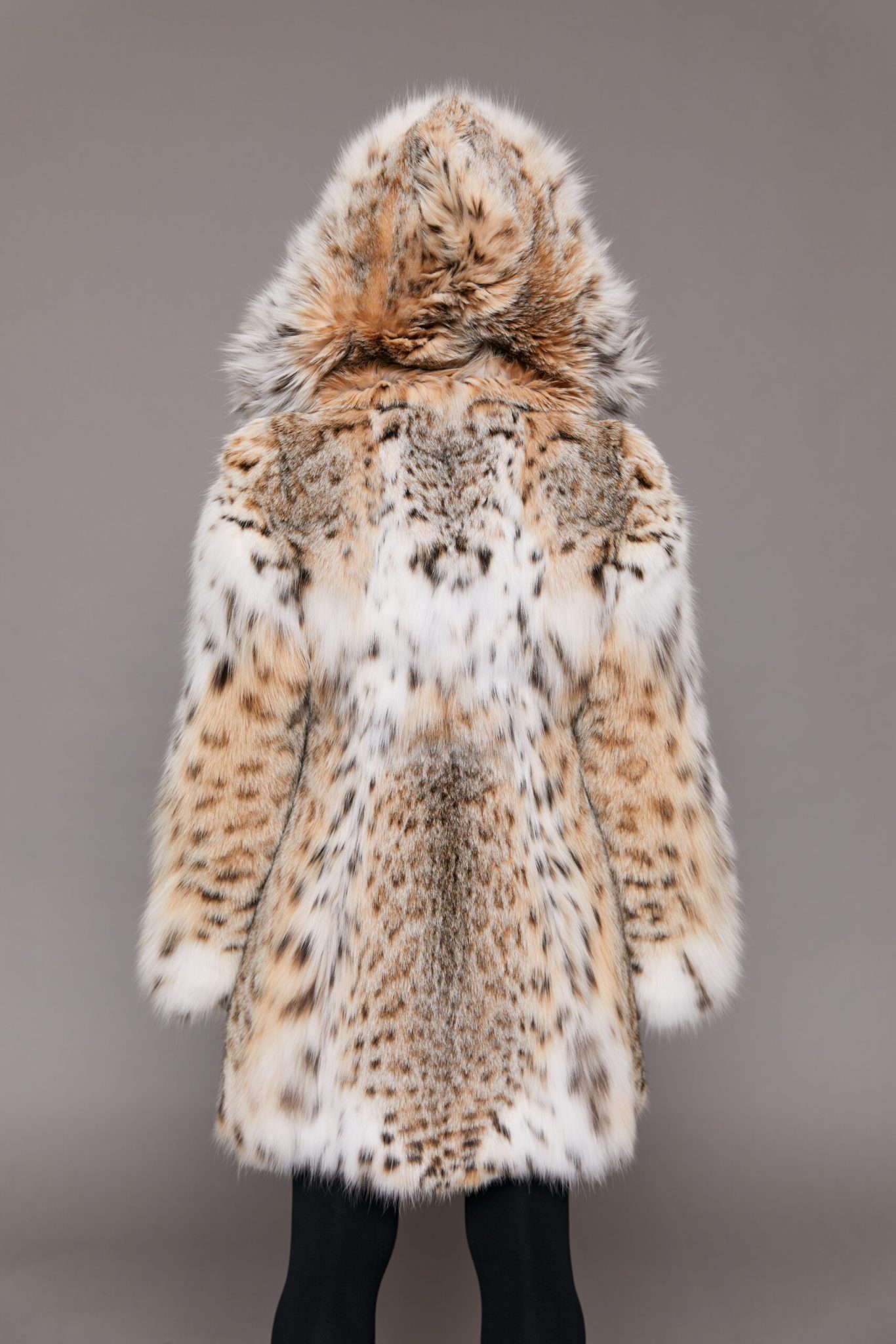 Rear view of a woman wearing a fur coat with the hood up facing a grey background.