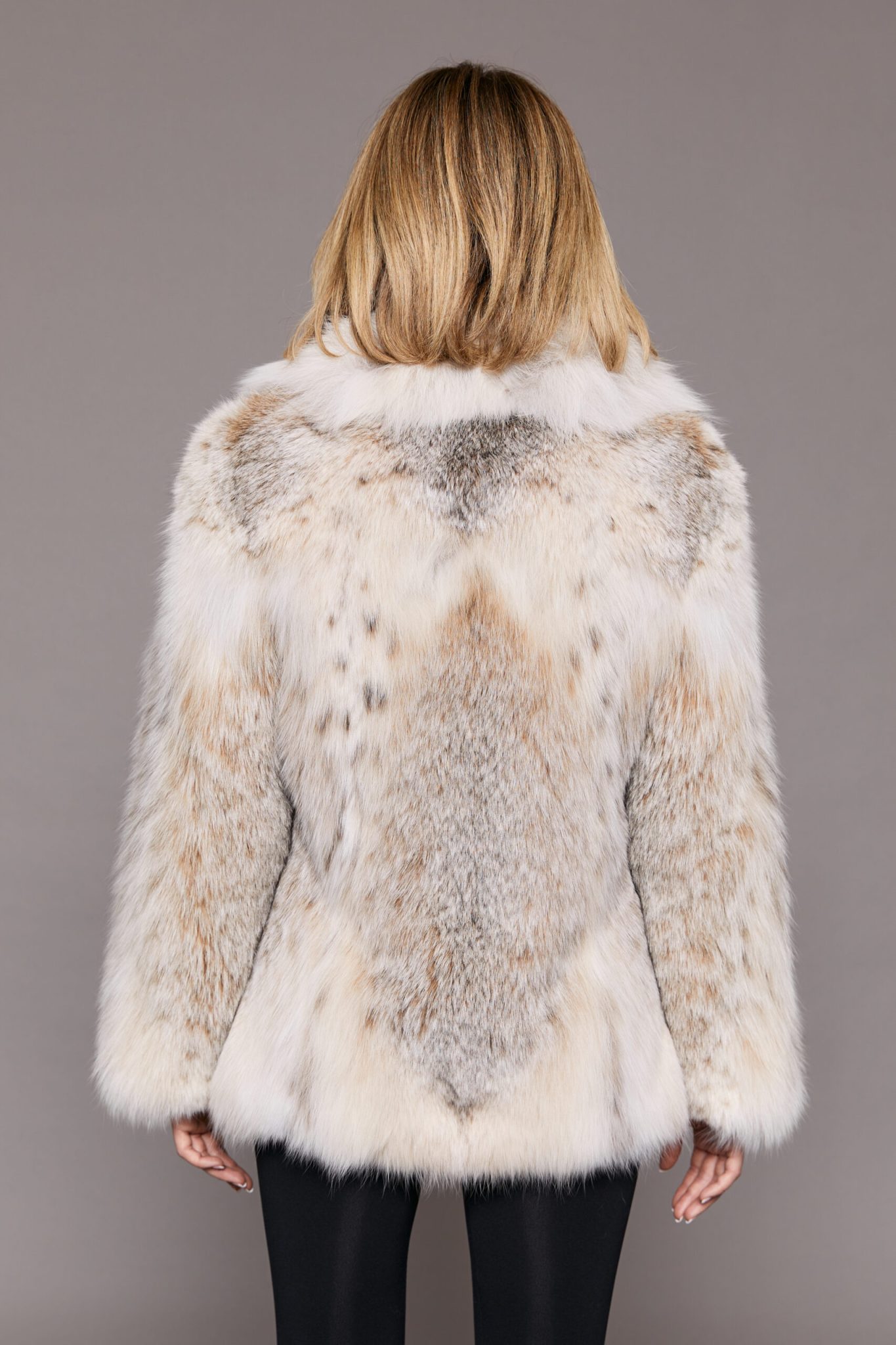 Rear shot of a woman wearing a Canadian lynx jacket facing a grey backdrop