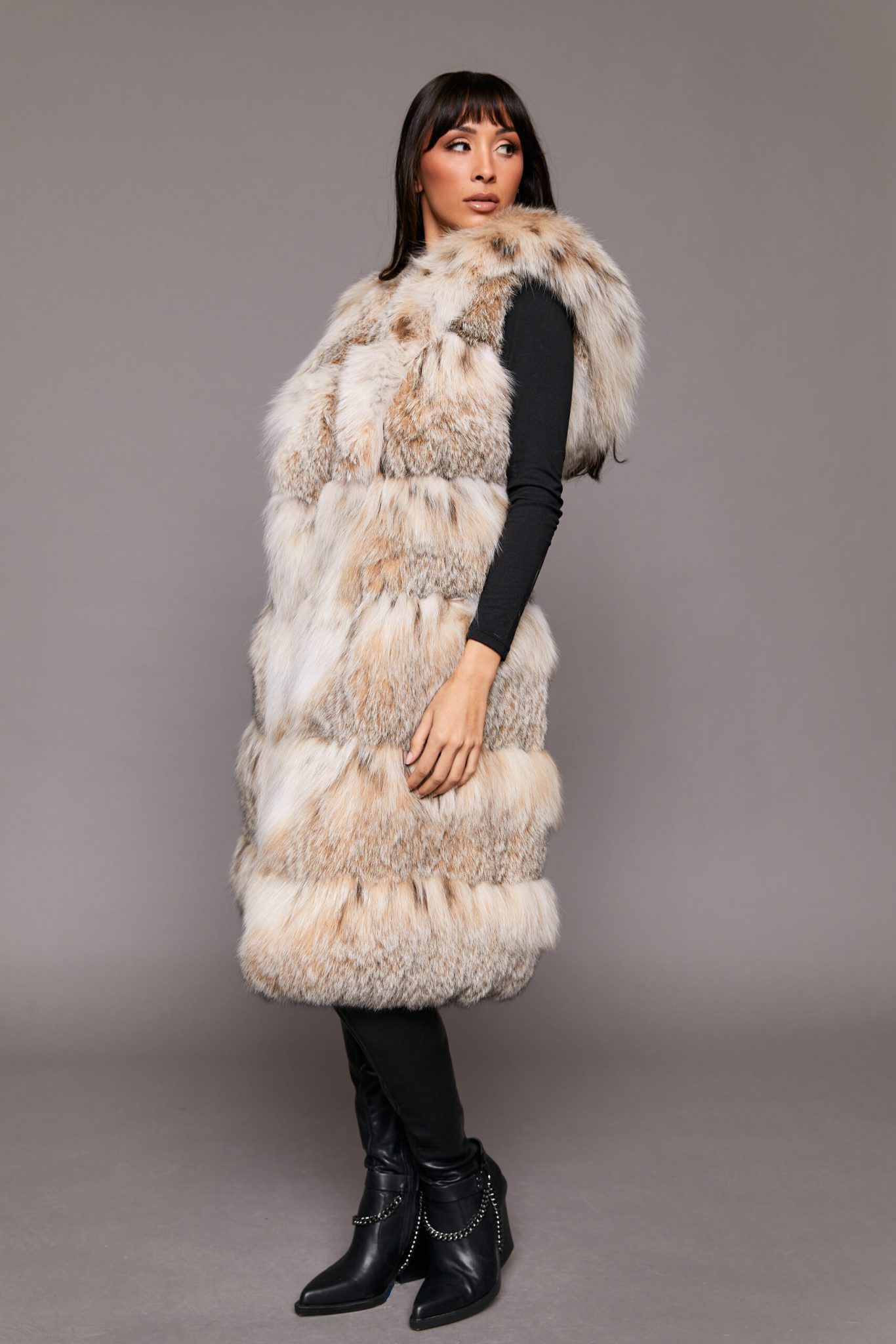 Profile shot of a woman wearing a fur vest standing in front of a grey background, the woman is looking to the left