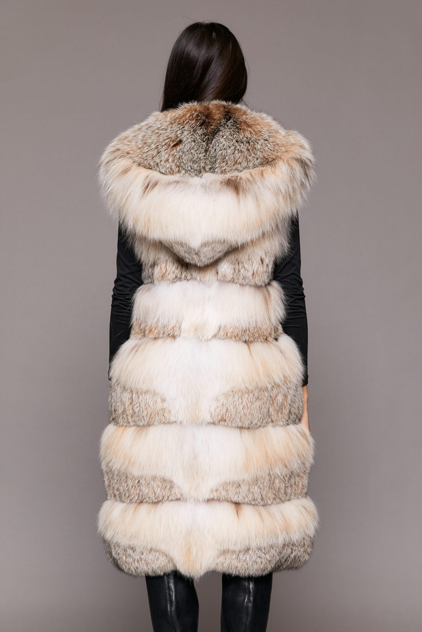 Rear view of a woman wearing a fur vest facing a grey background