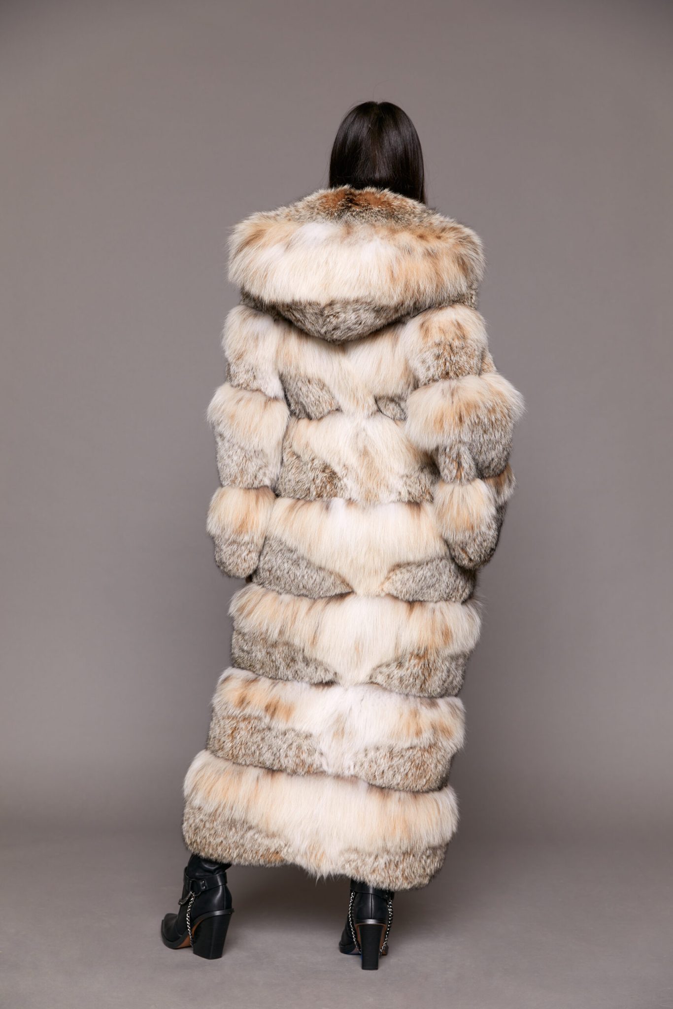 Rear view of a woman wearing a full length fur coat facing a grey background