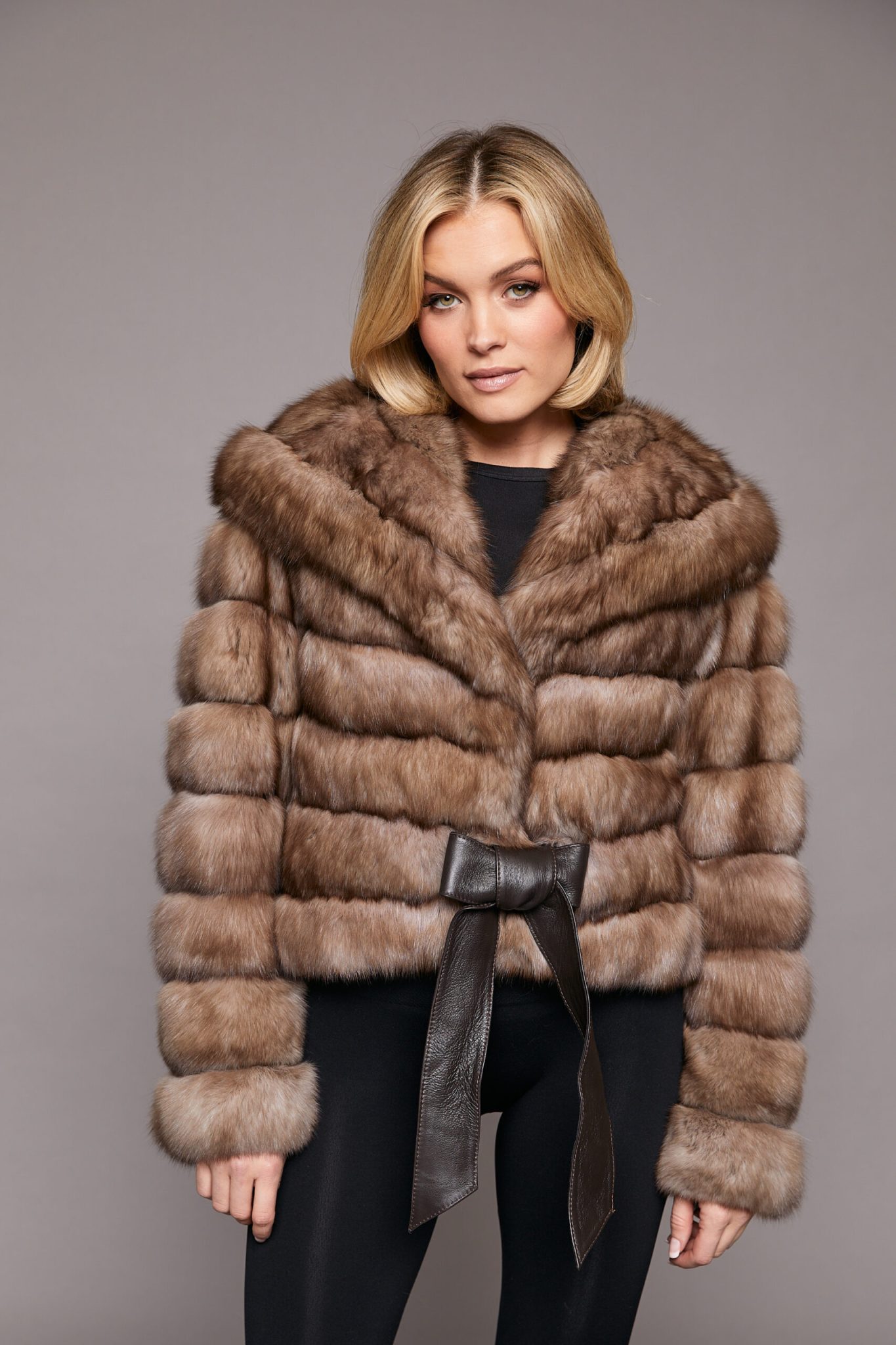 Frontal view of a woman wearing a sable jacket standing in front of a grey background