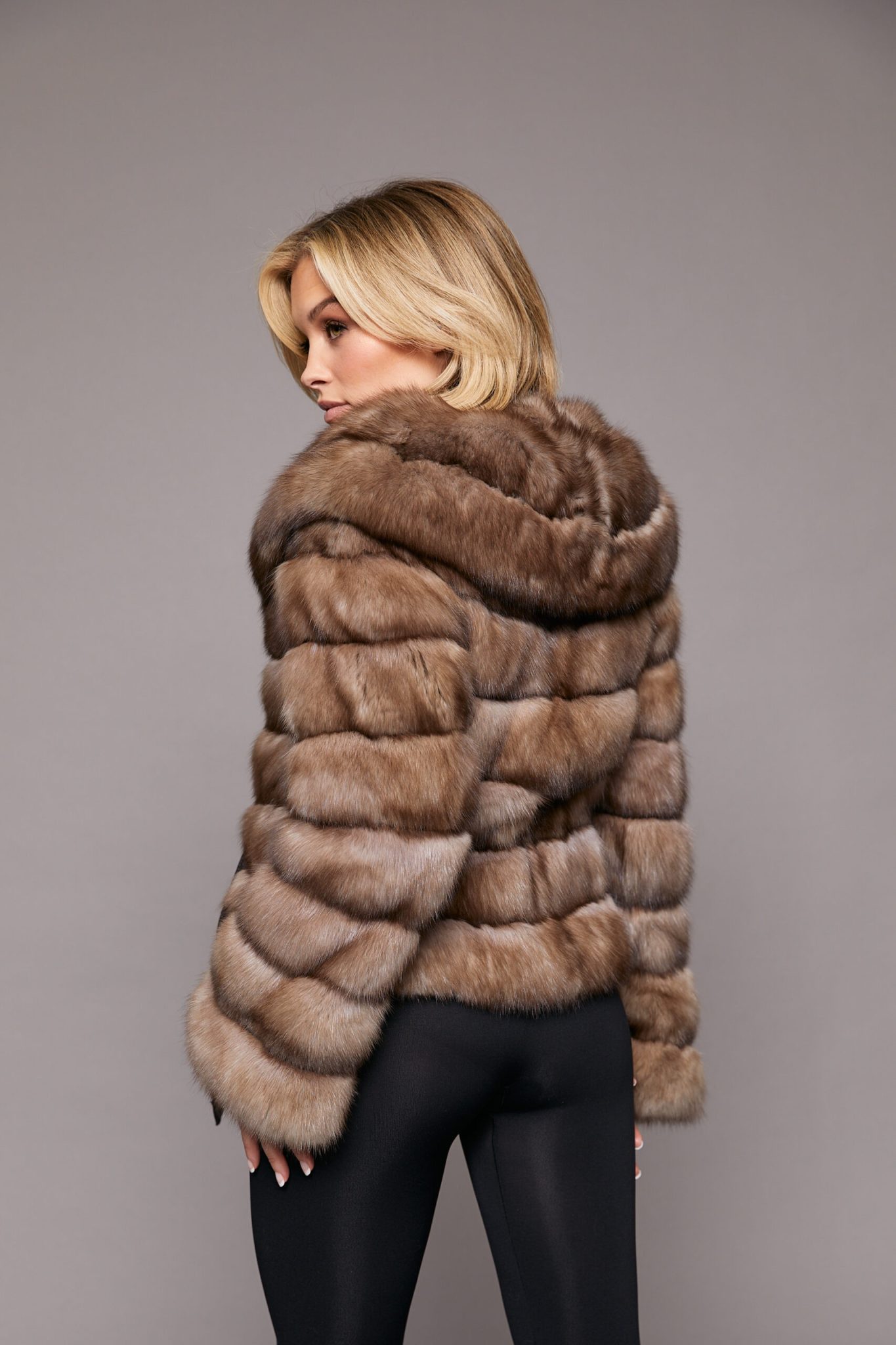 Rear view of a woman wearing a sable jacket standing towards a grey background