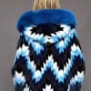 SFGPHOTOPIADAY1_LOOK10_0042 Rear view of a woman in a blue-colored mink fur coat with a fox-trimmed hood facing a grey background.