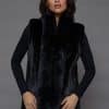Frontal view of a woman in a black mink fur vest standing in front of a grey background