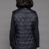 Rear view of a woman in a mink fur vest with the shell side out standing against a grey background
