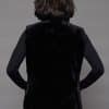 Rear view of a woman in a mink fur vest with the fur side out facing a grey background