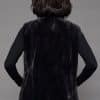 Rear view of a woman in a mink fur vest with the fur side out facing a grey background