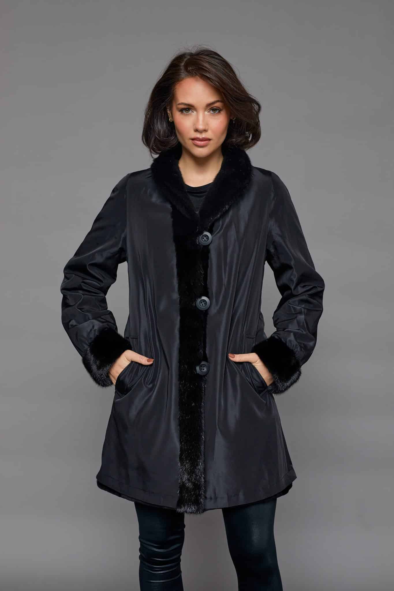 9954BLACK-2 Frontal view of a woman in a black coat with the rainwear side out standing in front of a grey background