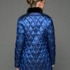 Reverse view of a woman in a reversible coat with the blue quilted shell side out, she both arms positioned straight down to her sides and is standing facing a grey background