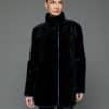 Frontal view of a woman in a reversible coat with the black fur side out, she has both arms at her sides and is standing in front of a grey background