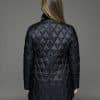 Rear view of a woman in a reversible coat with the black quilted shell side out, she has both arms at her sides and is facing a grey background