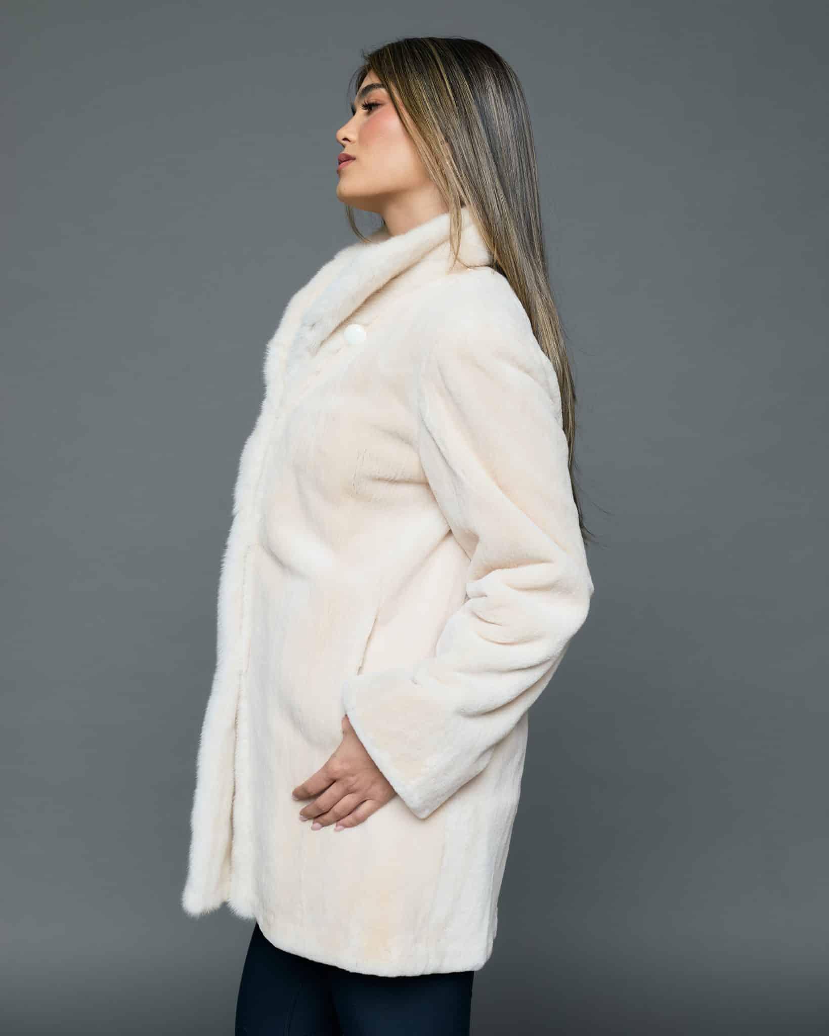 ECOMMWOMENS20256624 Profile view of a woman in a white coat with the fur side out and her left thumb in the pocket standing in front of a grey background