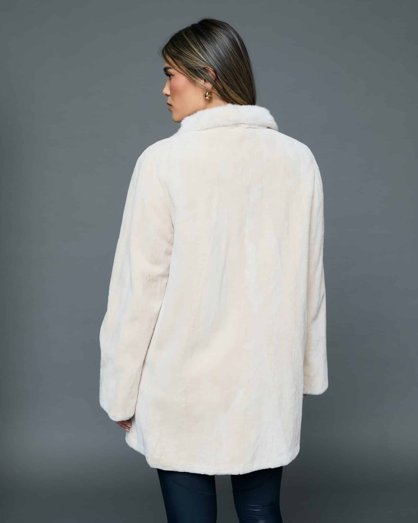 ECOMMWOMENS20256635 Rear view of a woman in a white coat with the fur side out standing in front of a grey background