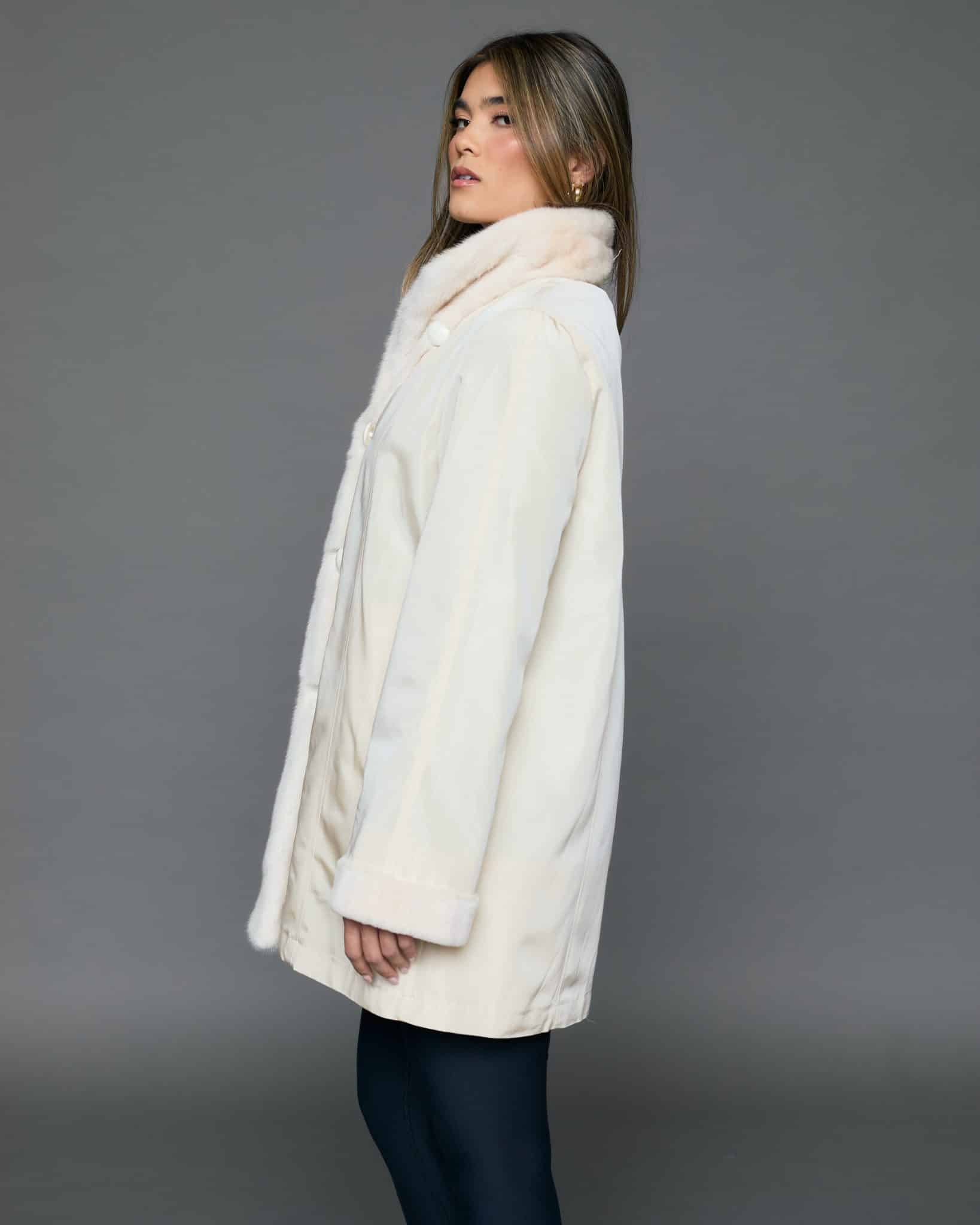 ECOMMWOMENS20256976 Profile view of a woman in a white coat with the fur side out standing in front of a grey background