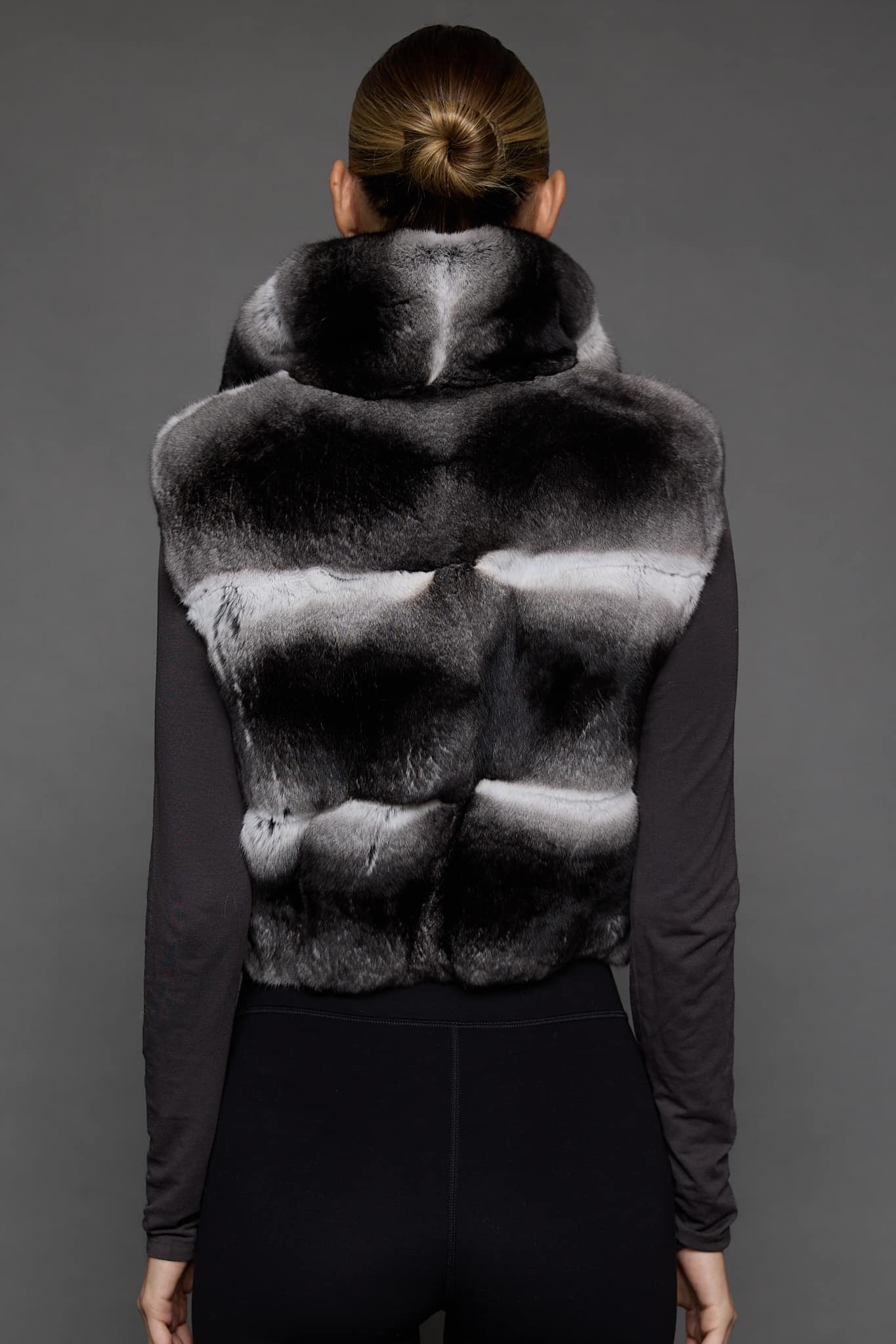 the back of a woman in a grey vest against a grey wall