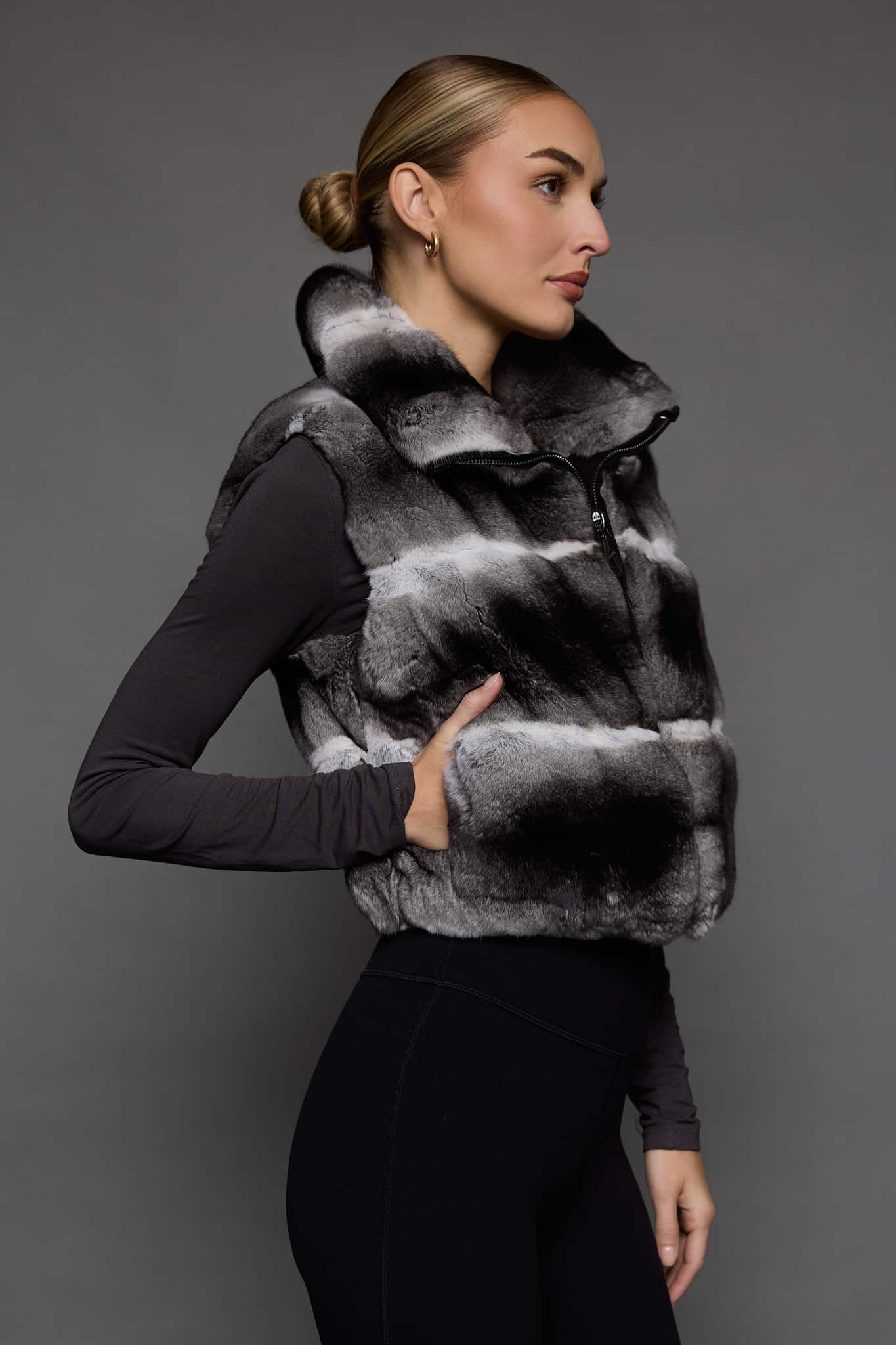 the side of a woman in a grey vest against a grey wall