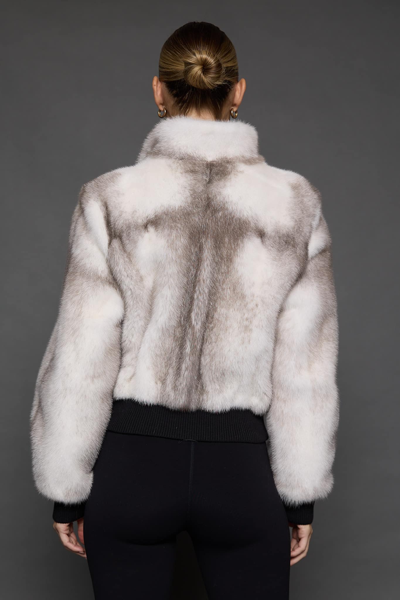 ATHANASIA CROSS MINK JACKET BACK Rear view of a woman in a white jacket against a grey background